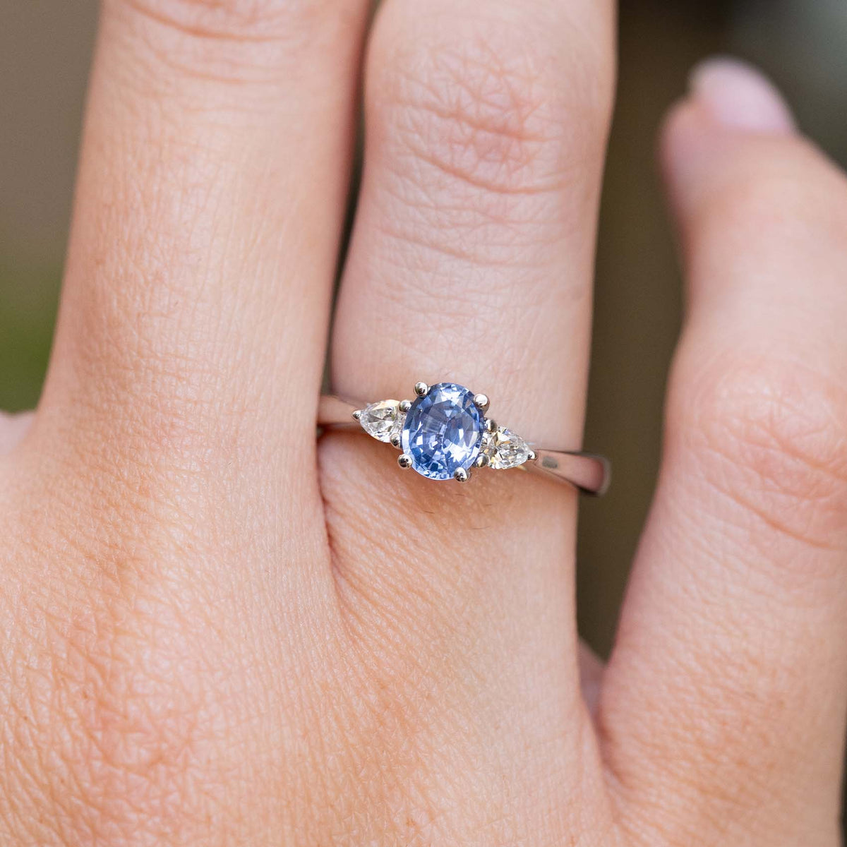A vintage-inspired light blue sapphire and diamond three-stone engagement ring worn on the finger.