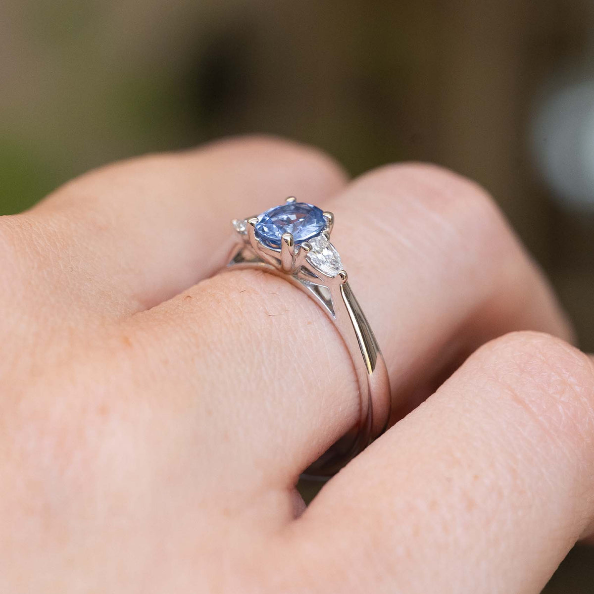 Close-up side detail of a vintage-inspired light blue sapphire and diamond three-stone engagement ring worn on the finger.