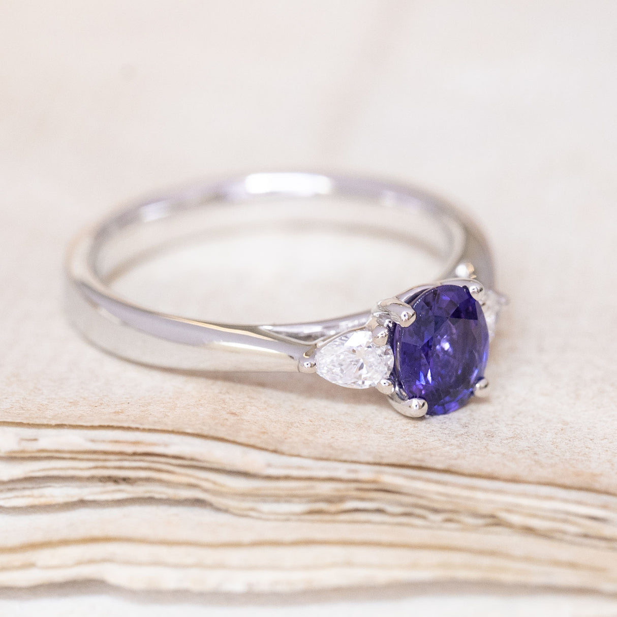 A vintage-inspired, indigo sapphire & diamond three-stone engagement ring in platinum showing the flanked diamond.