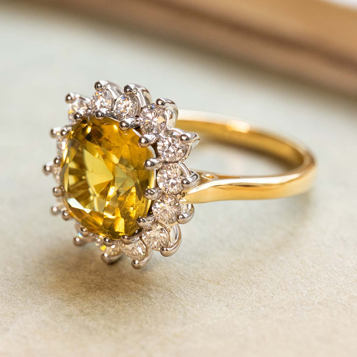 A three-quarter profile of an antique-inspired, yellow sapphire and diamond cluster displayed on a book.
