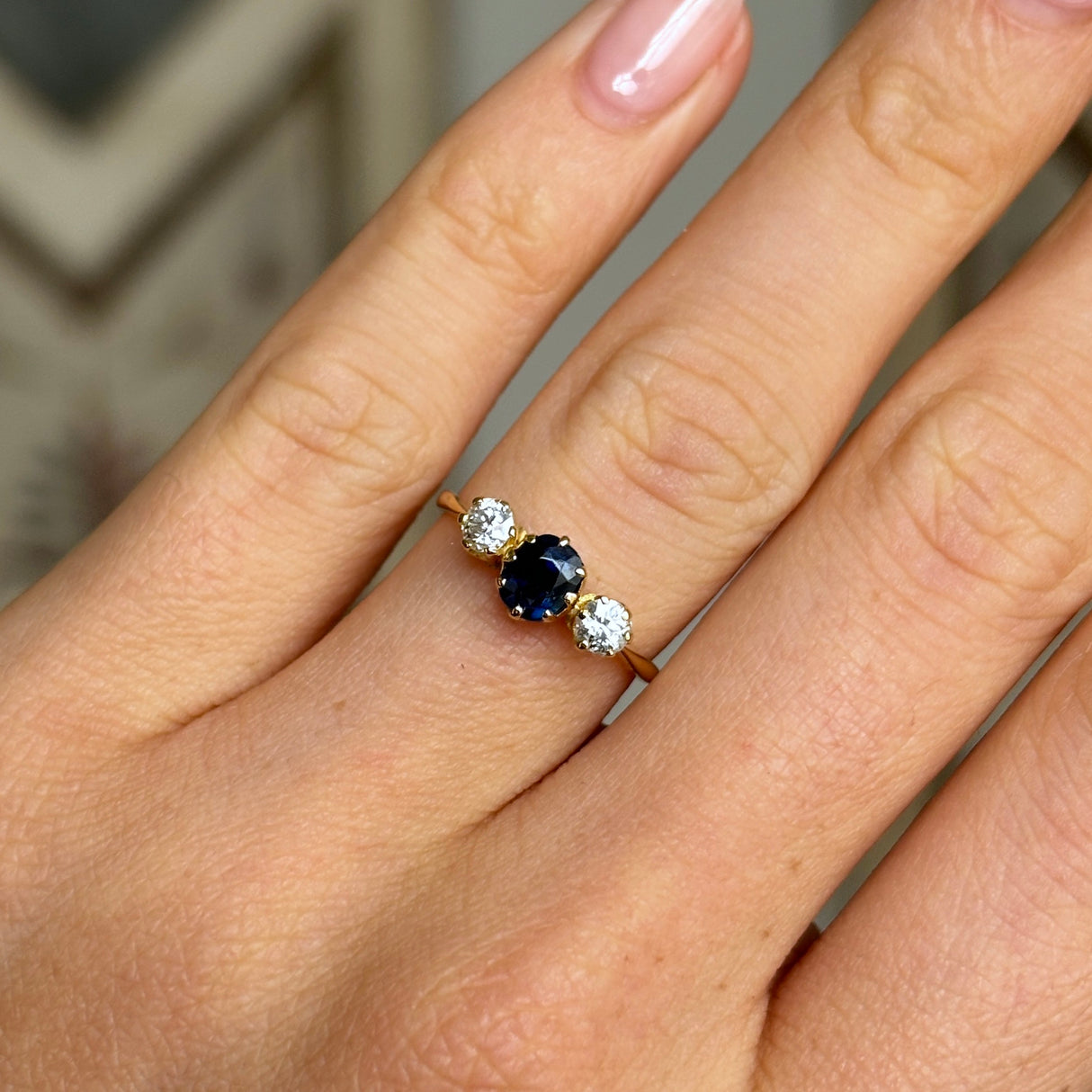 Antique, Edwardian sapphire and diamond three-stone engagement ring worn on hand.
