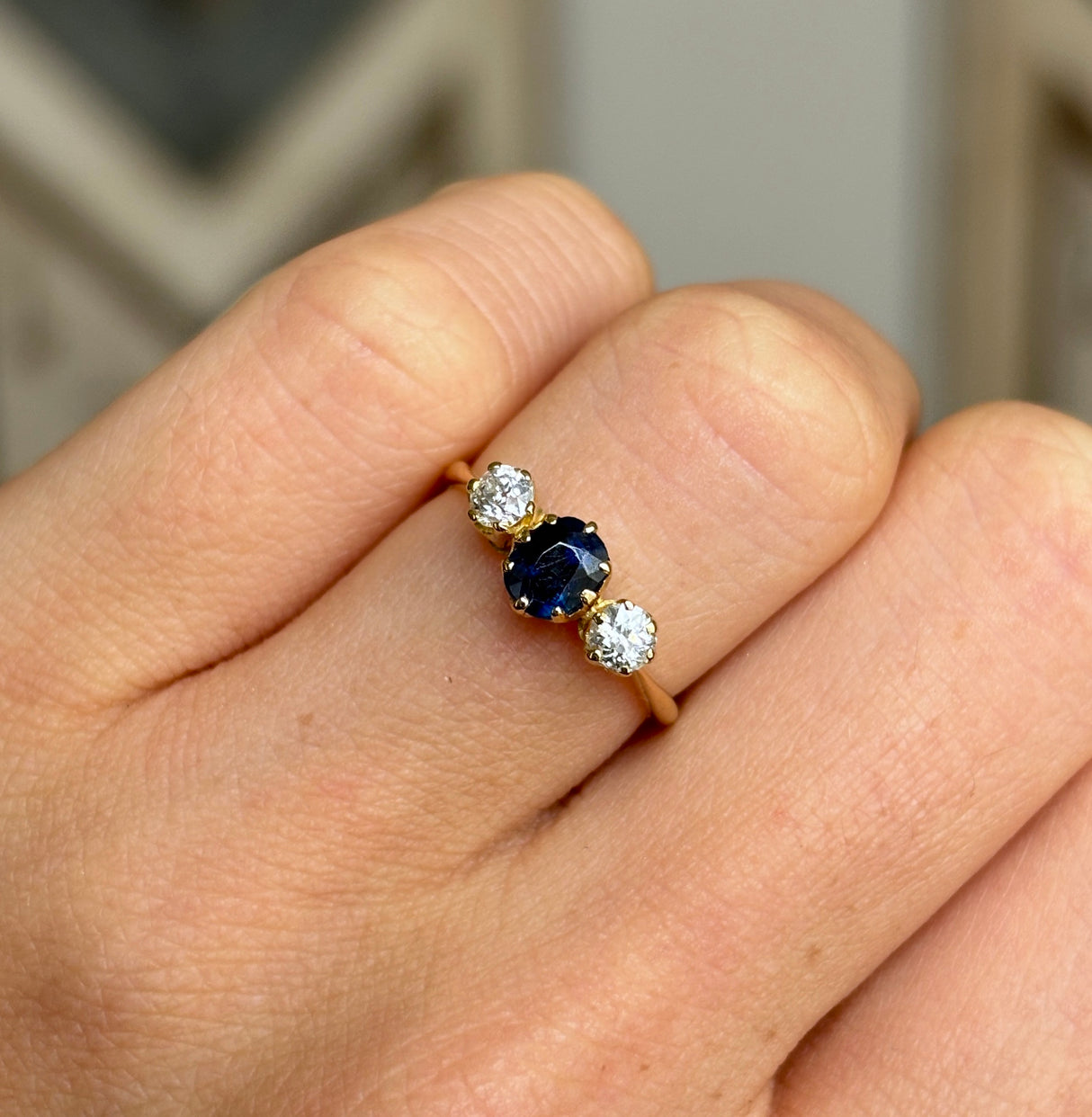 Antique, Edwardian sapphire and diamond three-stone engagement ring worn on hand.