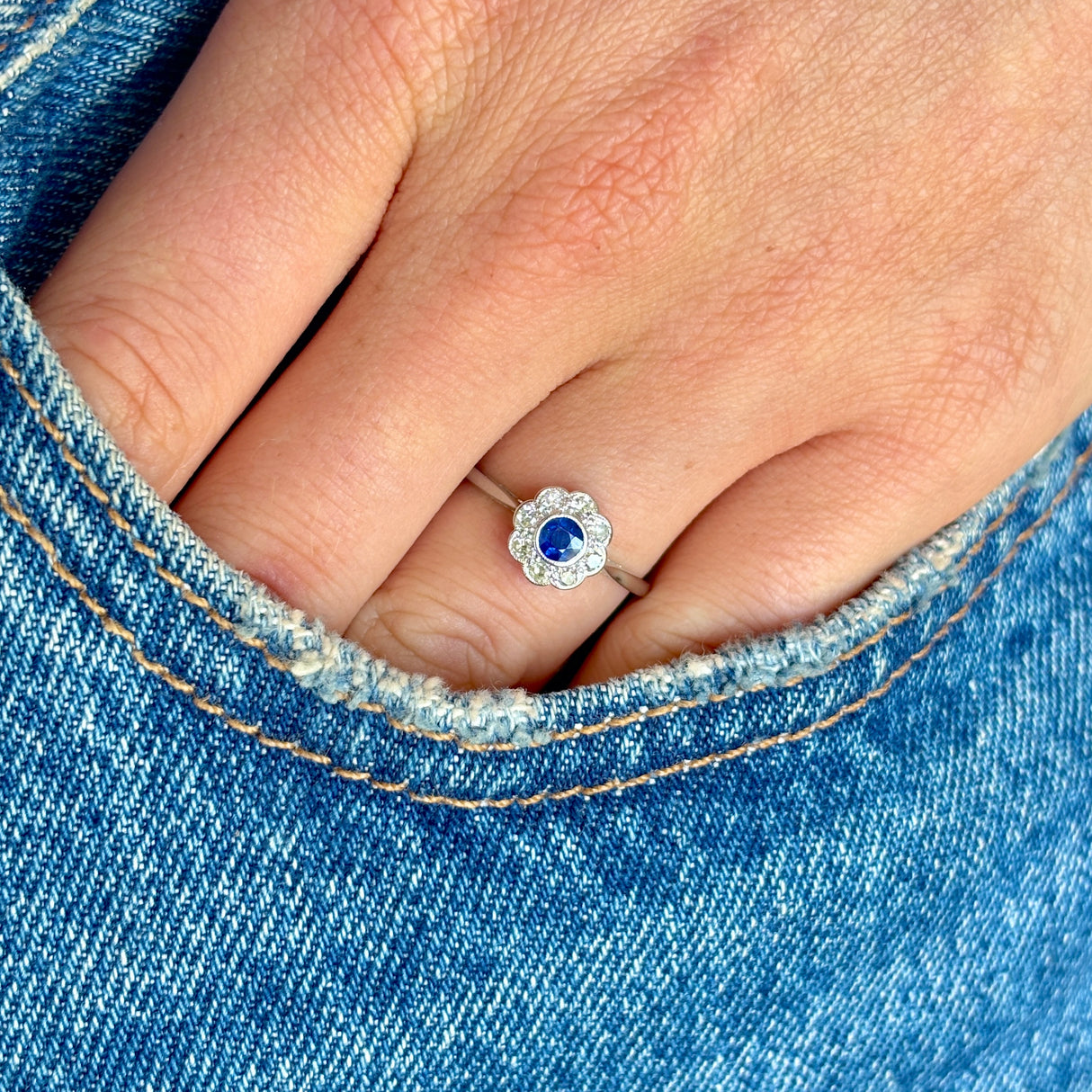 Close-up of a hand wearing a diamond and sapphire ring against a denim background