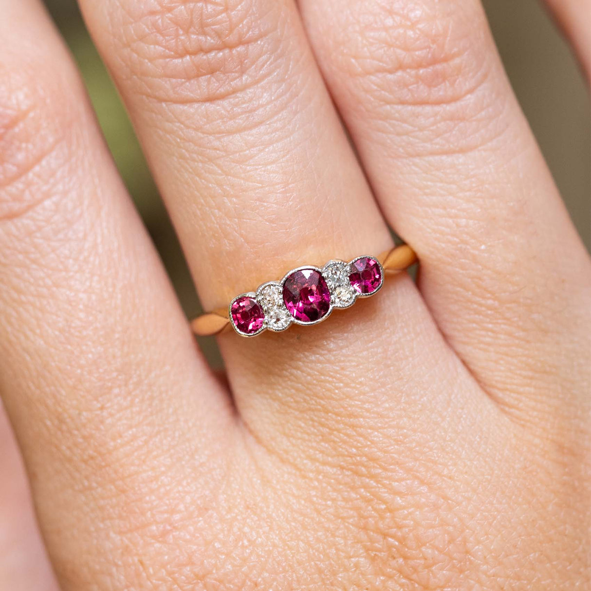 An antique Edwardian ruby and diamond five-stone engagement ring worn on the finger.