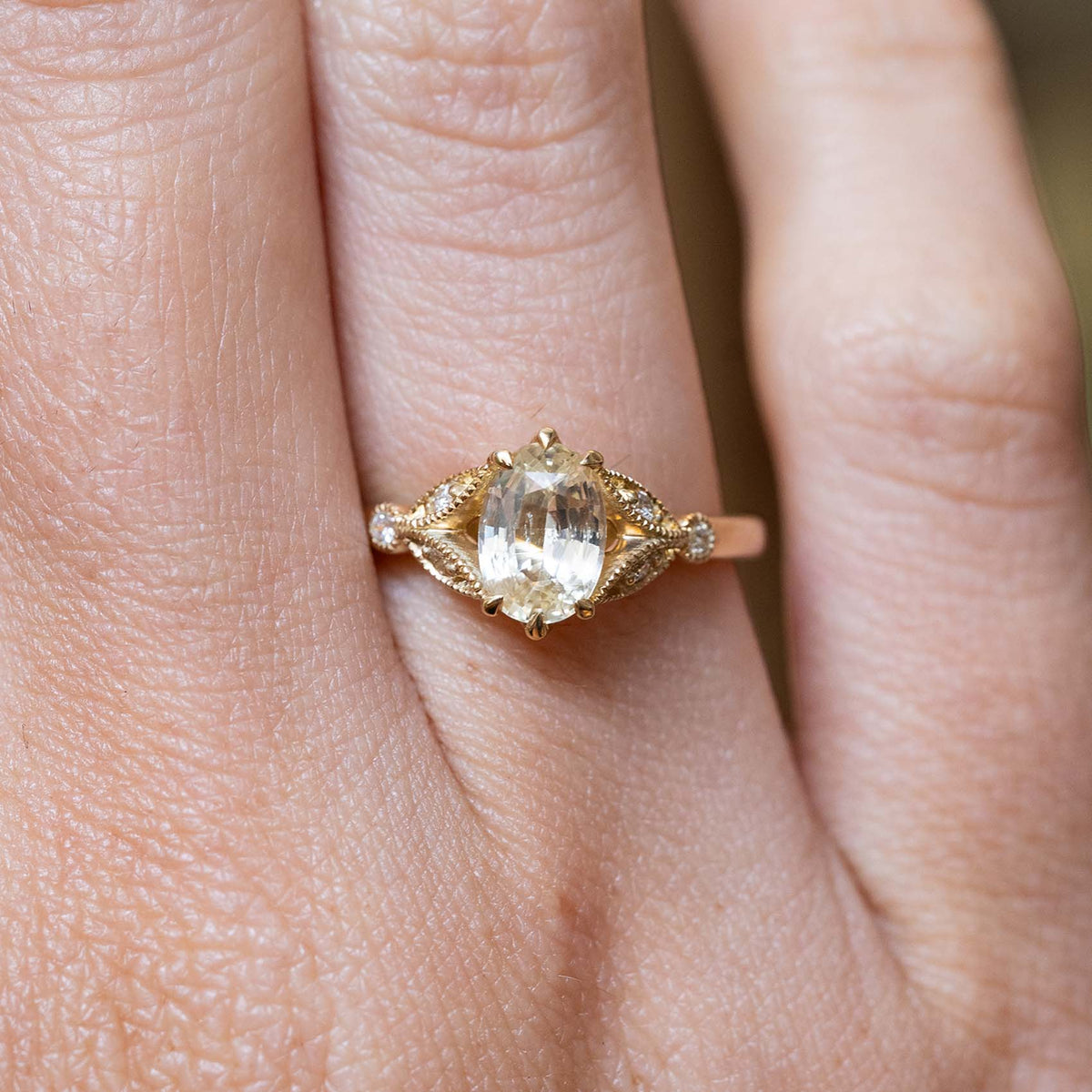 Antique-inspired oval-cut yellow sapphire and diamond engagement ring in yellow gold worn on the finger.