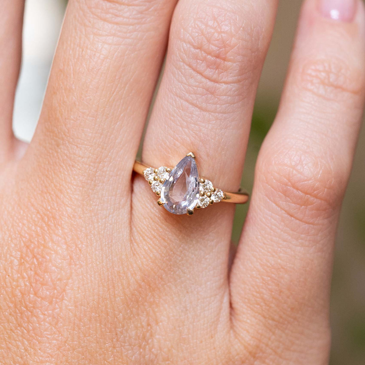 Vintage-inspired white pear-cut sapphire and diamond trefoil engagement ring in yellow gold worn on the finger.