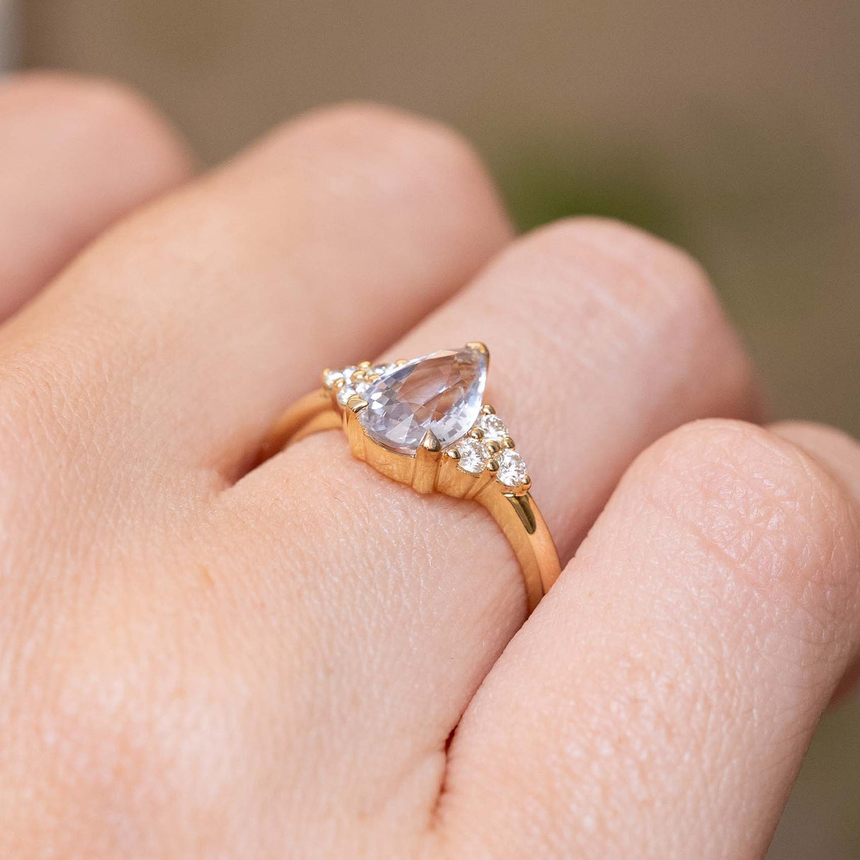 Close detail of a vintage-inspired white pear-cut sapphire engagement ring with a diamond trefoil setting in yellow gold.