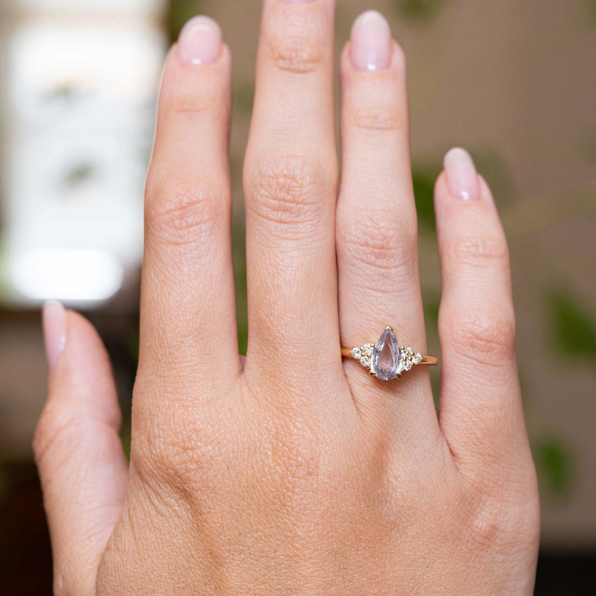 White pear-cut sapphire and diamond trefoil engagement ring in yellow gold displayed on the hand.