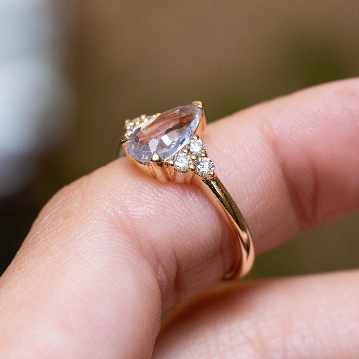 Detailed view of a white pear-cut sapphire and diamond trefoil engagement ring in polished yellow gold.