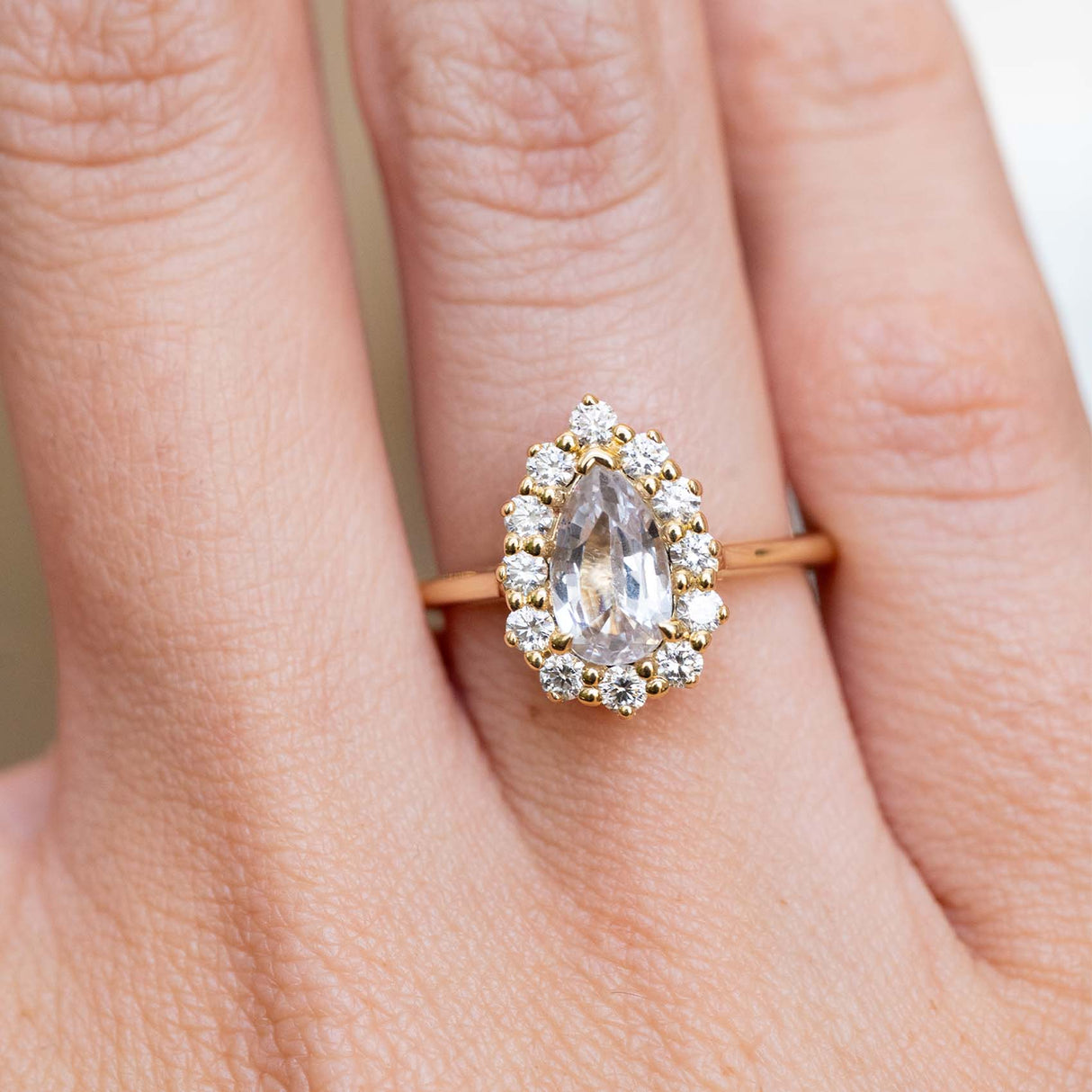 A vintage-inspired white sapphire and diamond cluster engagement ring in yellow gold worn on the finger.