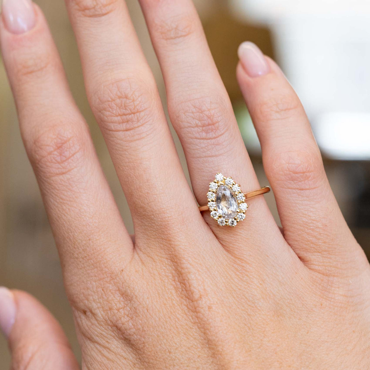 A vintage-inspired white sapphire and diamond engagement ring worn on the hand.