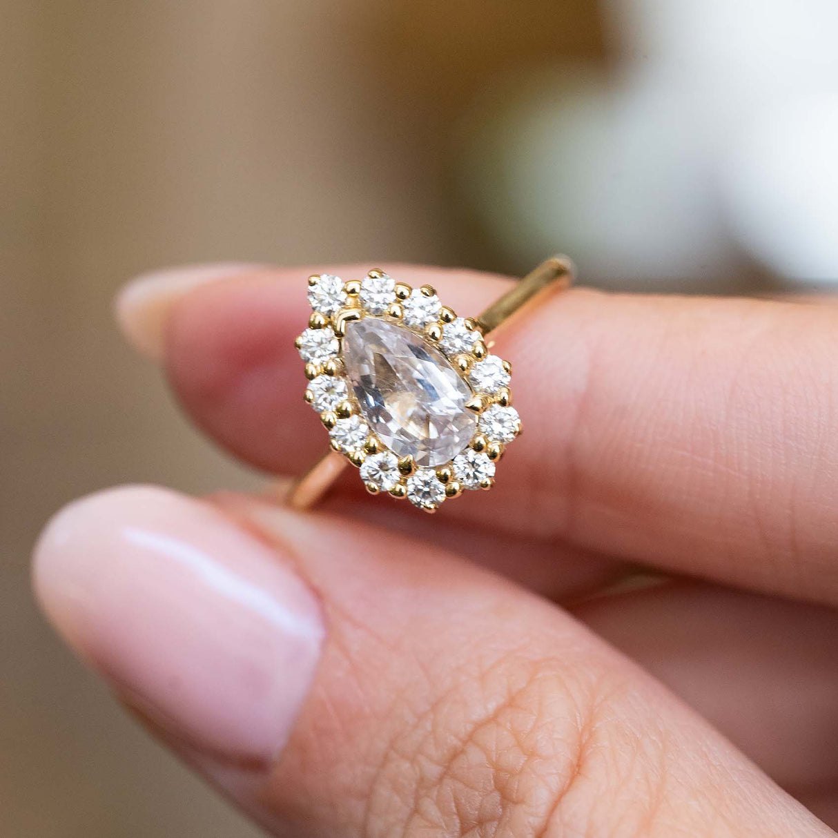 A vintage-inspired pear-cut white sapphire and diamond cluster ring held between the fingers.