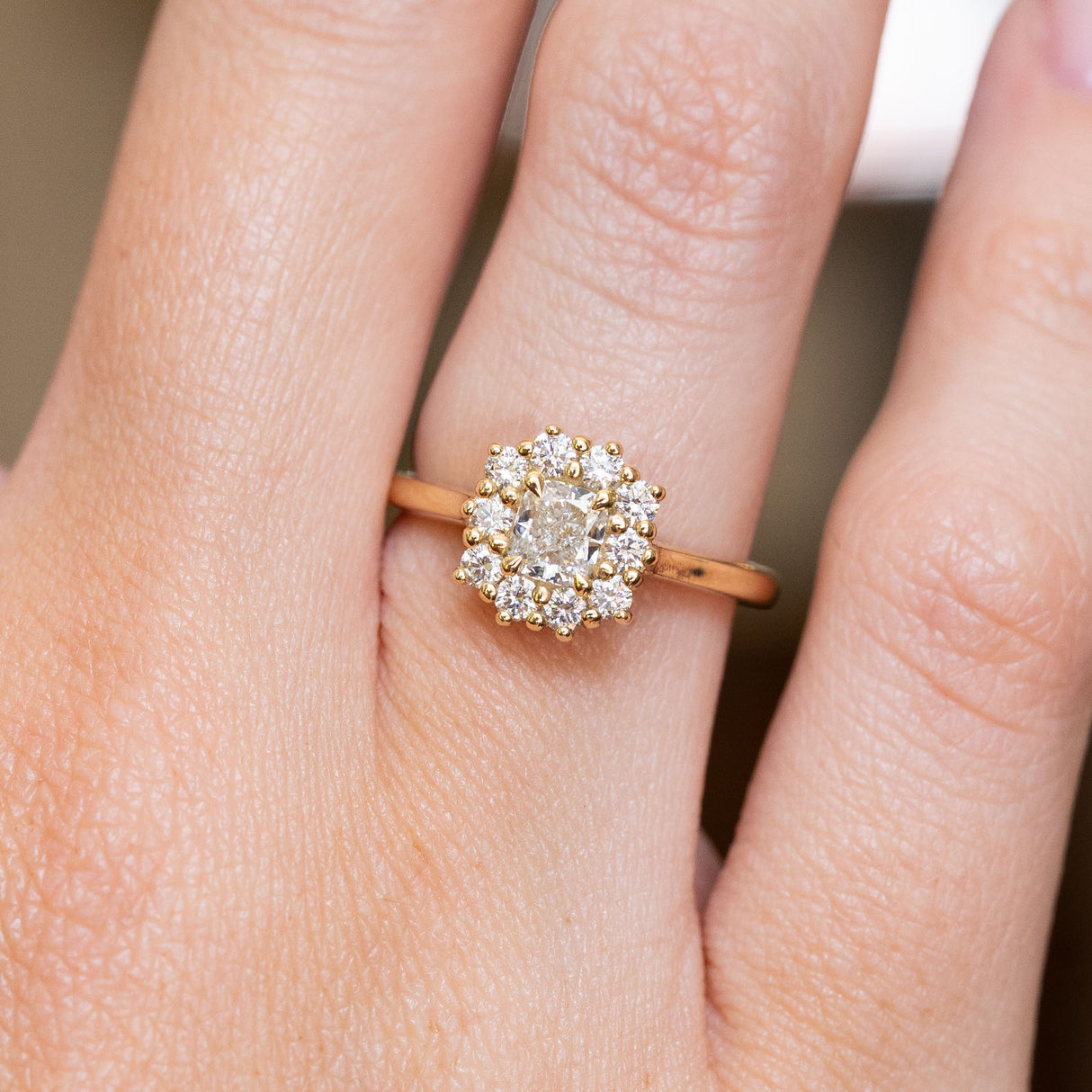 A close-up of an antique-inspired cushion-cut diamond halo engagement ring in yellow gold worn on a hand.