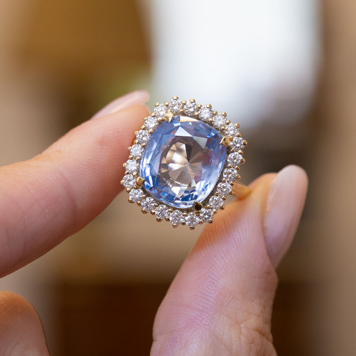 A vintage-inspired blue sapphire and diamond cluster ring in yellow gold held between the fingers.