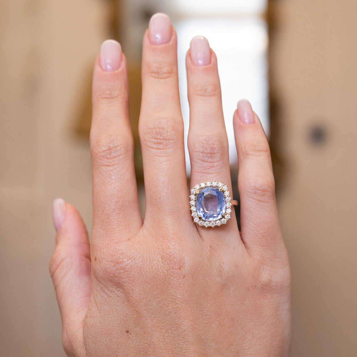 An antique-inspired light blue sapphire and diamond cluster ring in yellow gold worn on the hand.