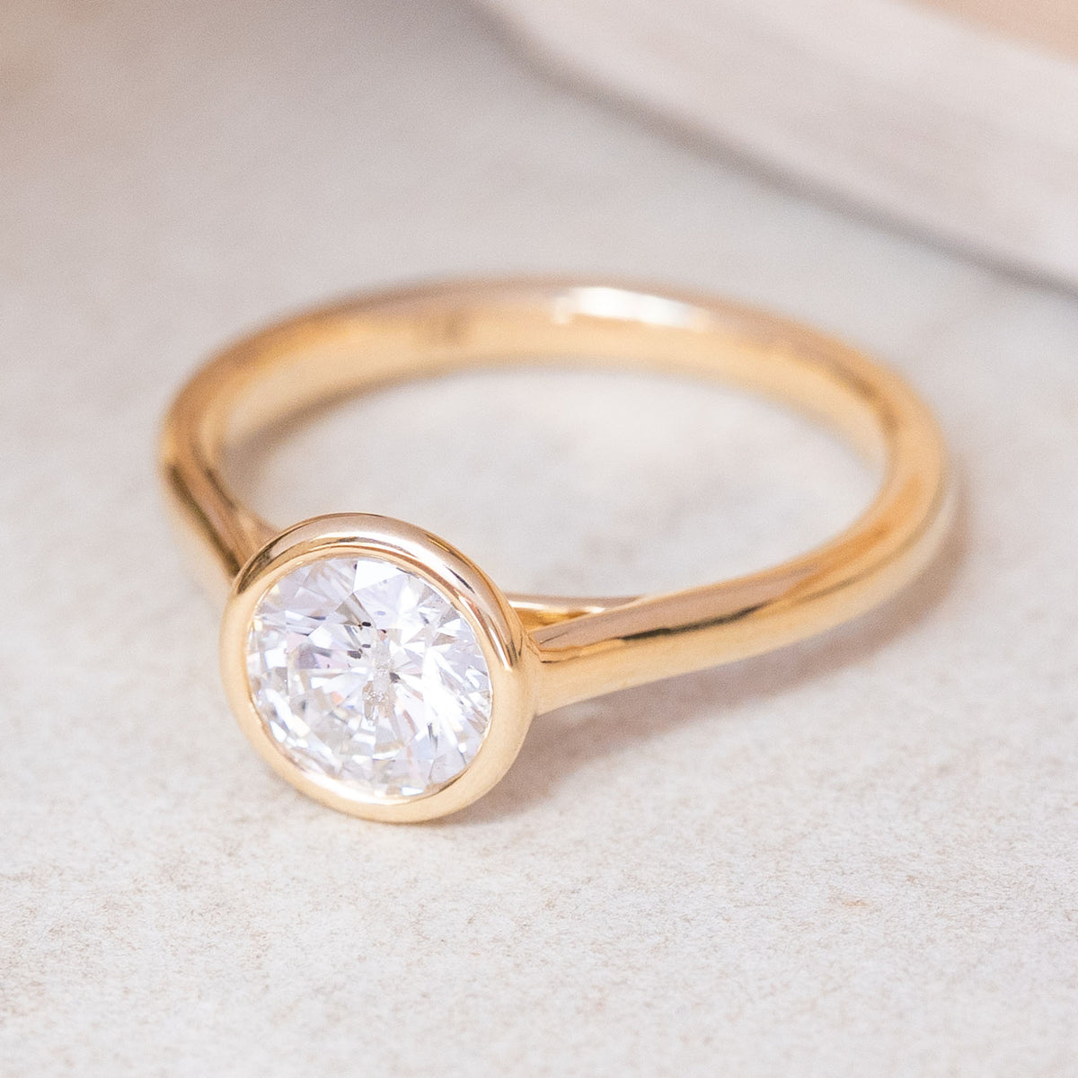 An Antique-inspired, 'salt and pepper' diamond rub-over solitaire engagement ring with a yellow gold band, resting on a light textured surface.