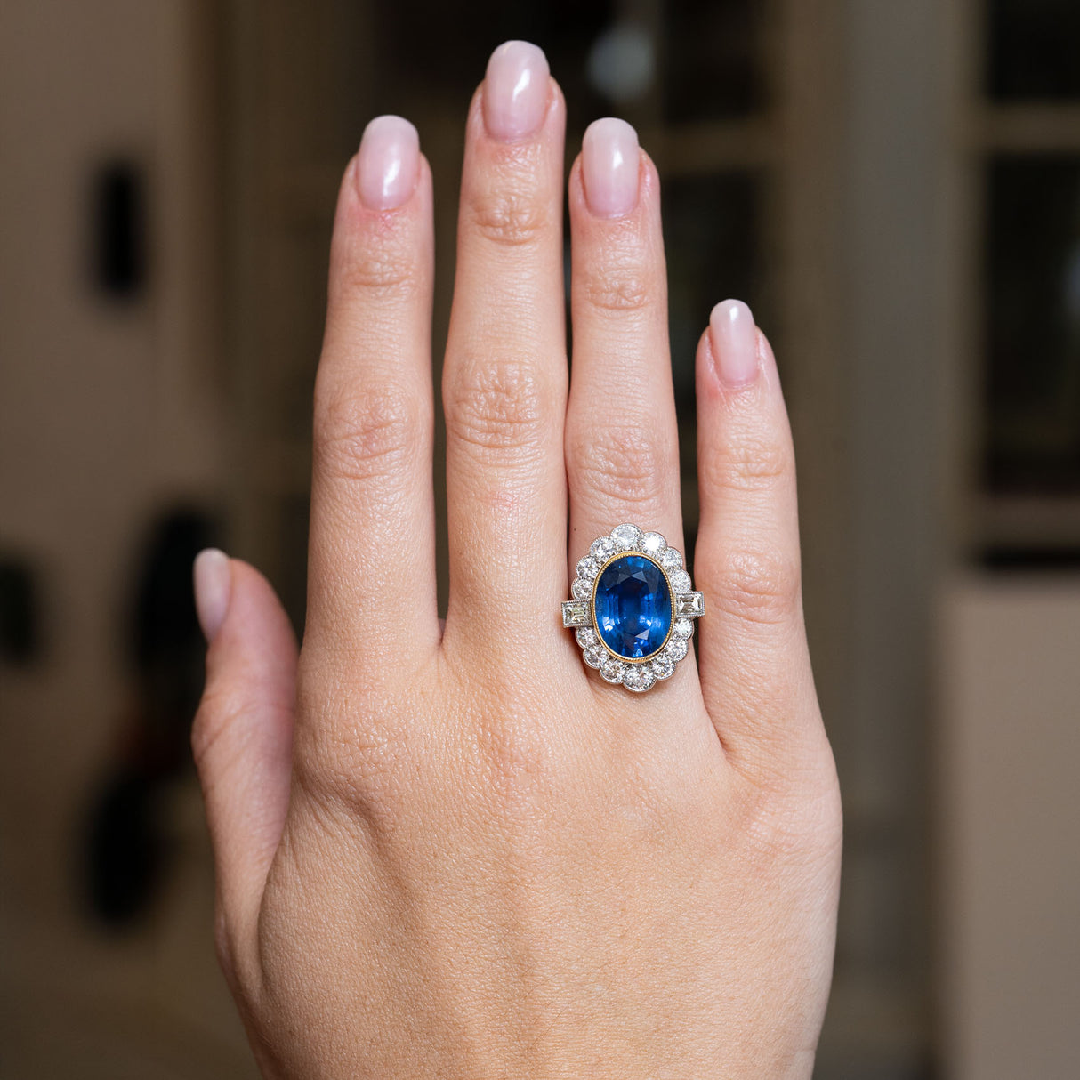 A vintage natural blue sapphire and diamond halo cluster ring worn on the hand.