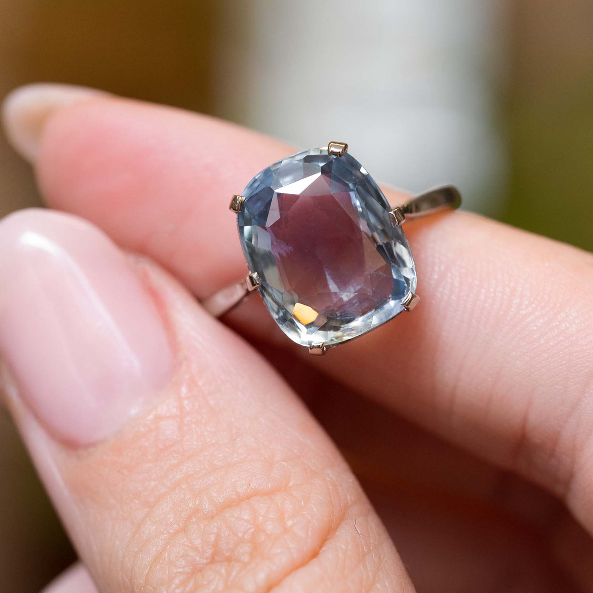 The sapphire solitaire ring held between fingers.