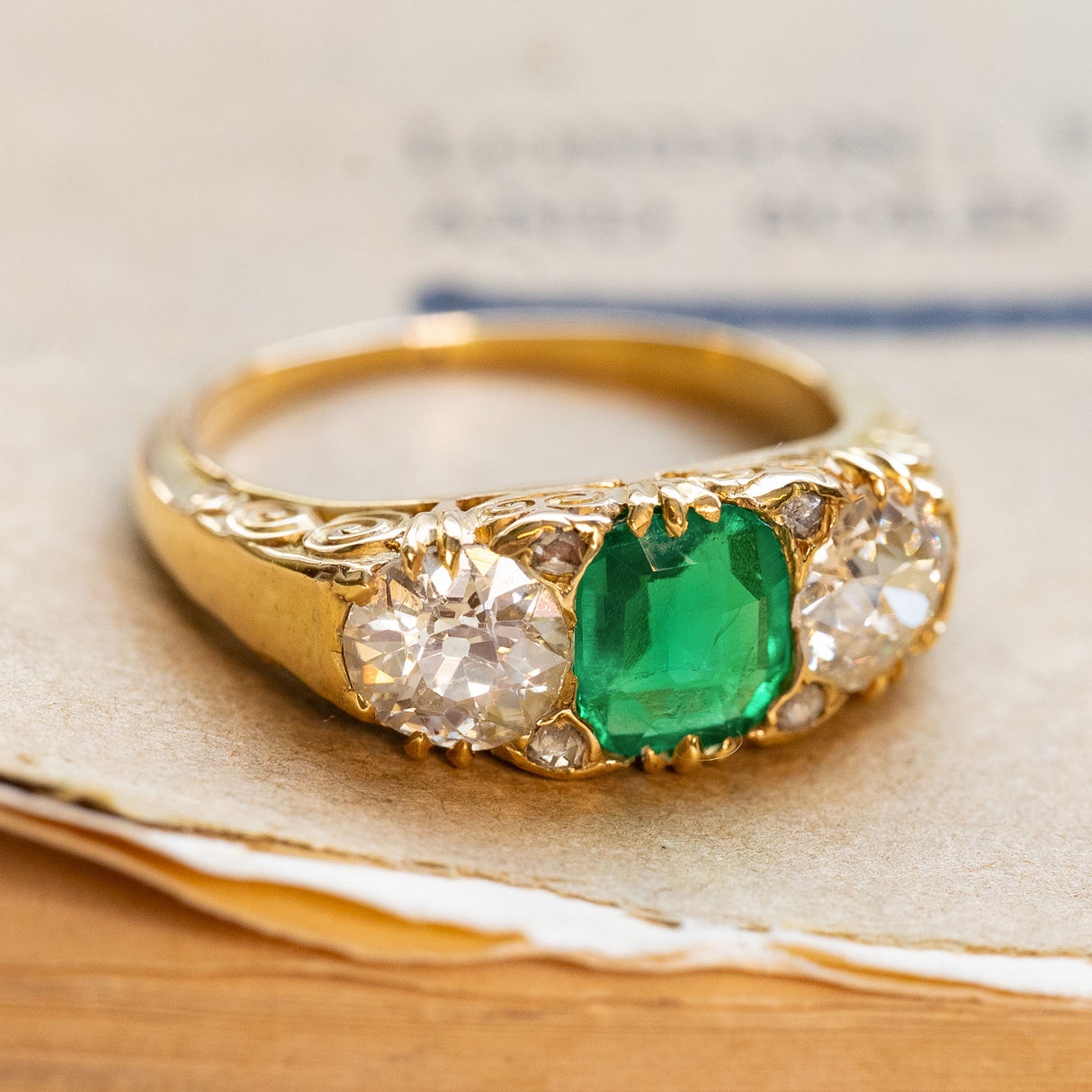 Antique Victorian emerald and diamond three-stone ring in yellow gold with decorative scroll work in the gallery.