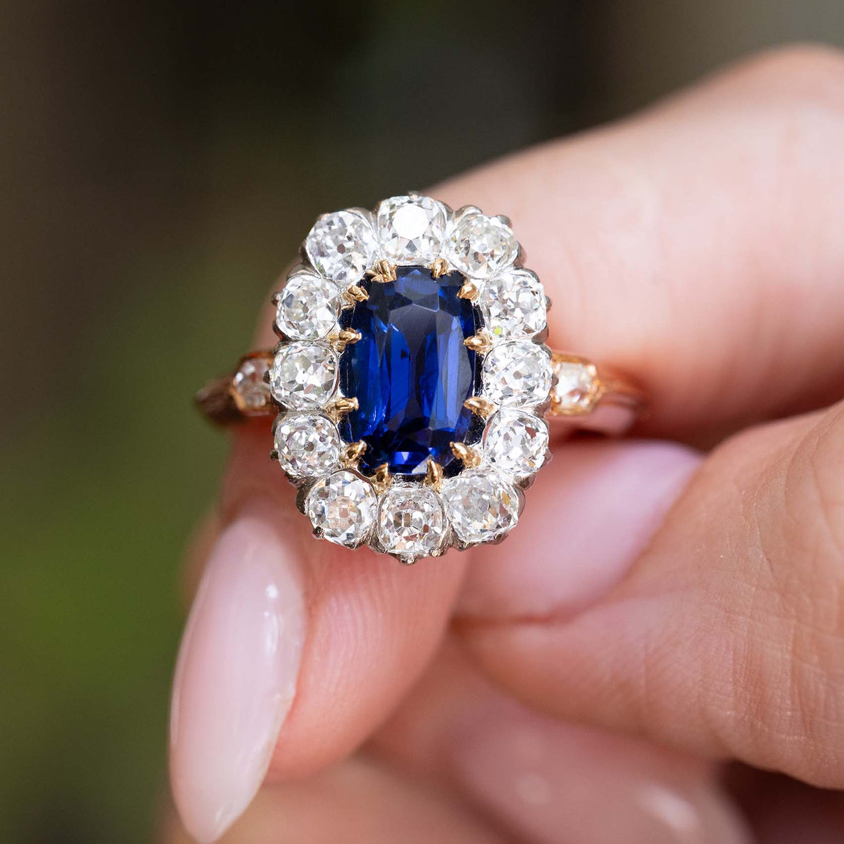 Close-up of an antique Jugendstil royal-blue sapphire and diamond cluster ring held between the fingers.