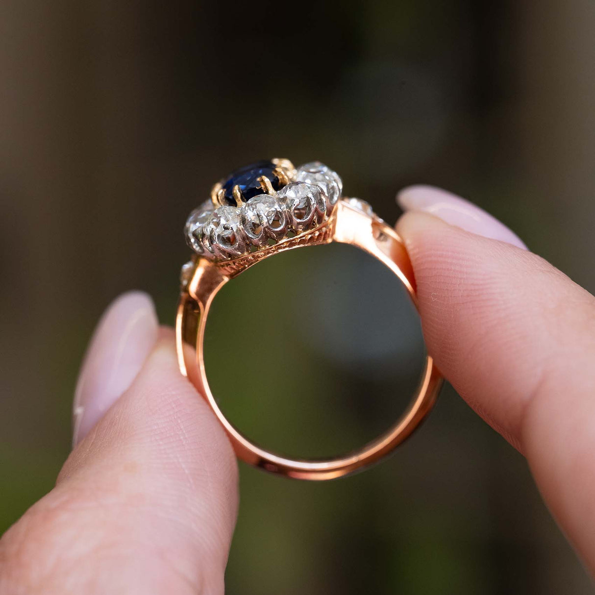 Side detail of an antique Jugendstil royal-blue sapphire and diamond cluster ring held between the fingers.