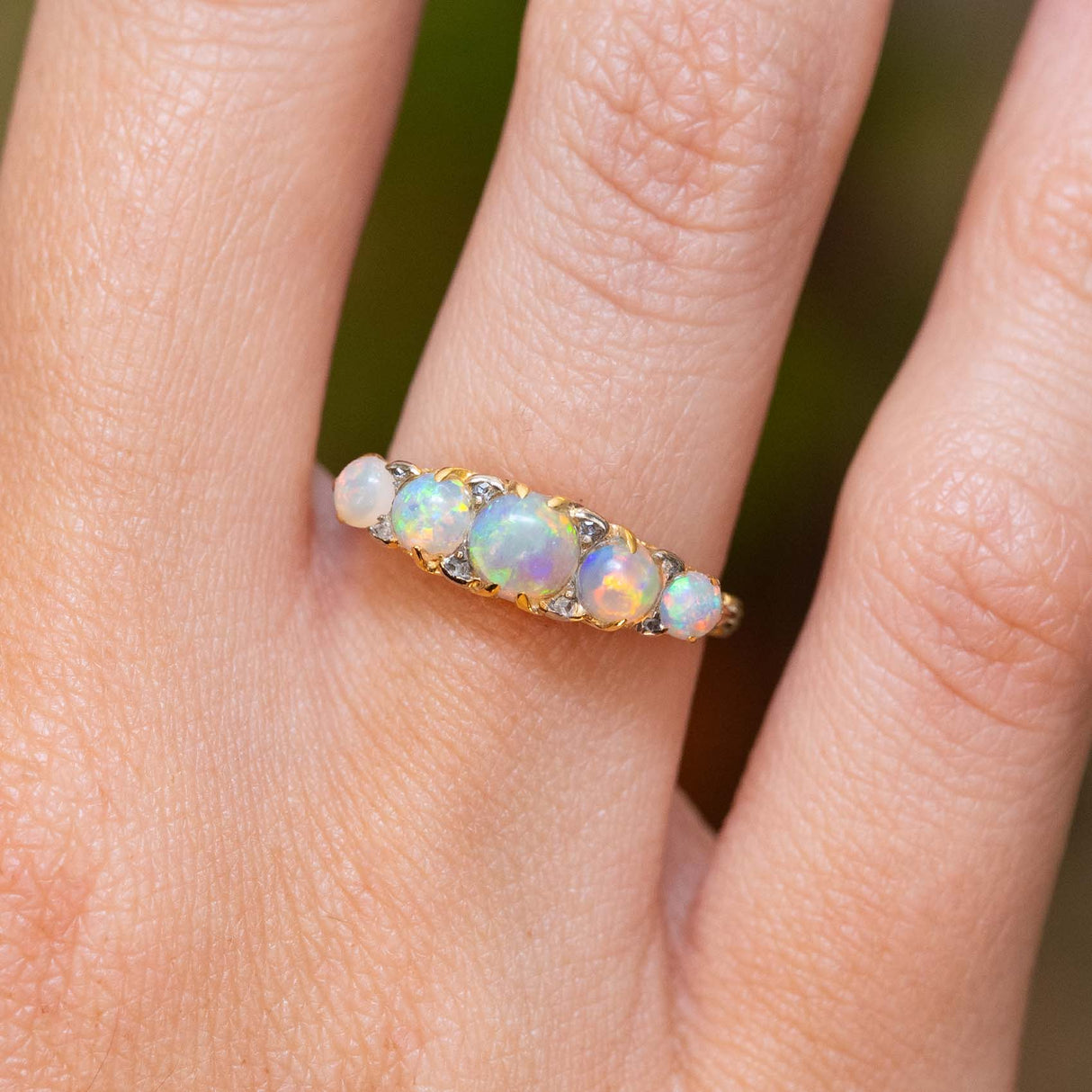 A close-up of an antique, Edwardian opal and diamond half-hoop ring in yellow gold. worn on a hand.
