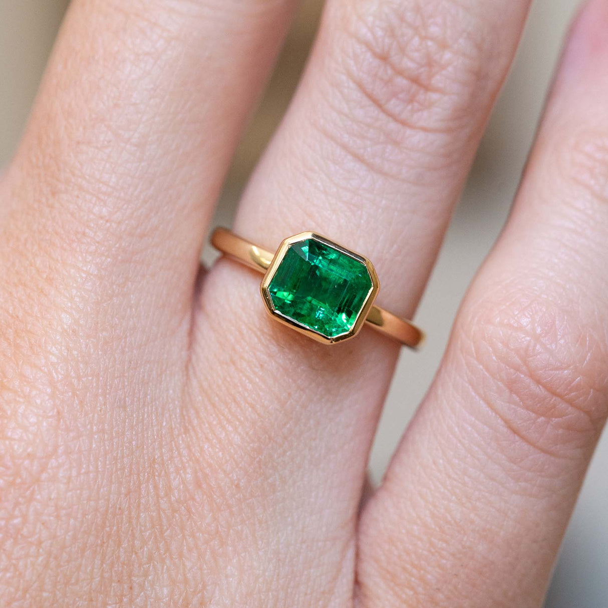 An antique-inspired emerald-cut emerald solitaire engagement ring in 14ct yellow gold worn on the finger.