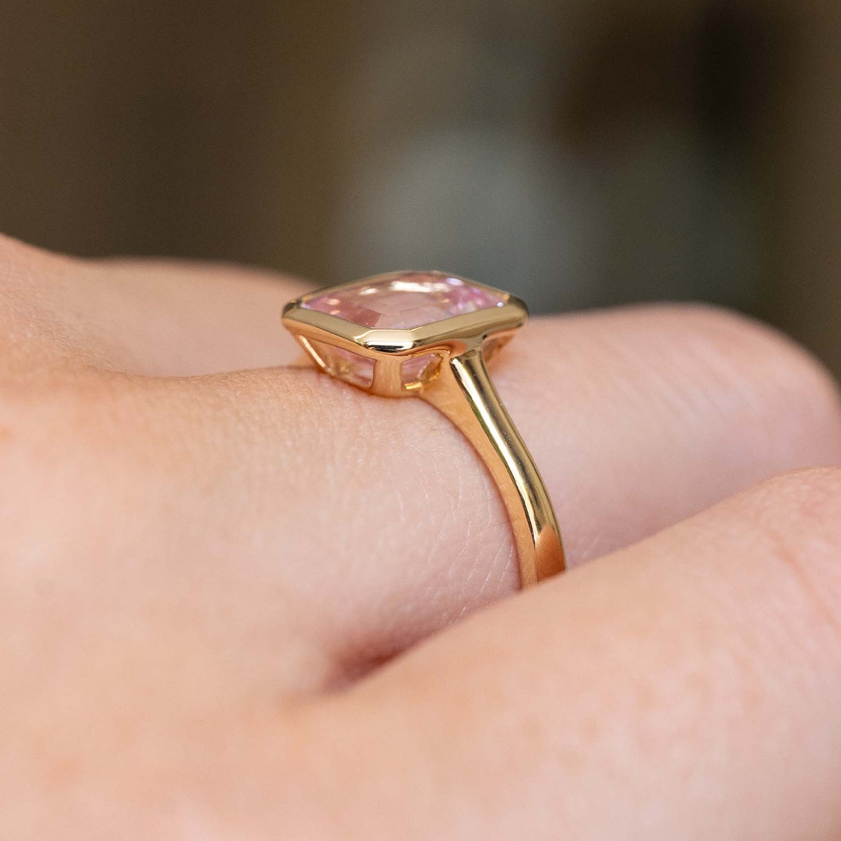 A close-up shot of a solitaire gold ring with a pink sapphire showing the side view of the ring with an open back.