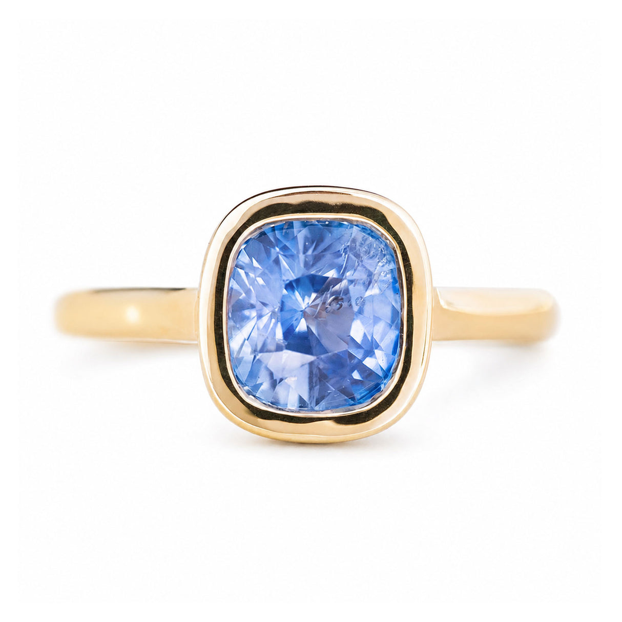 A close-up of an antique-inspired, blue coloured cushion-cut sapphire solitaire ring in yellow gold.