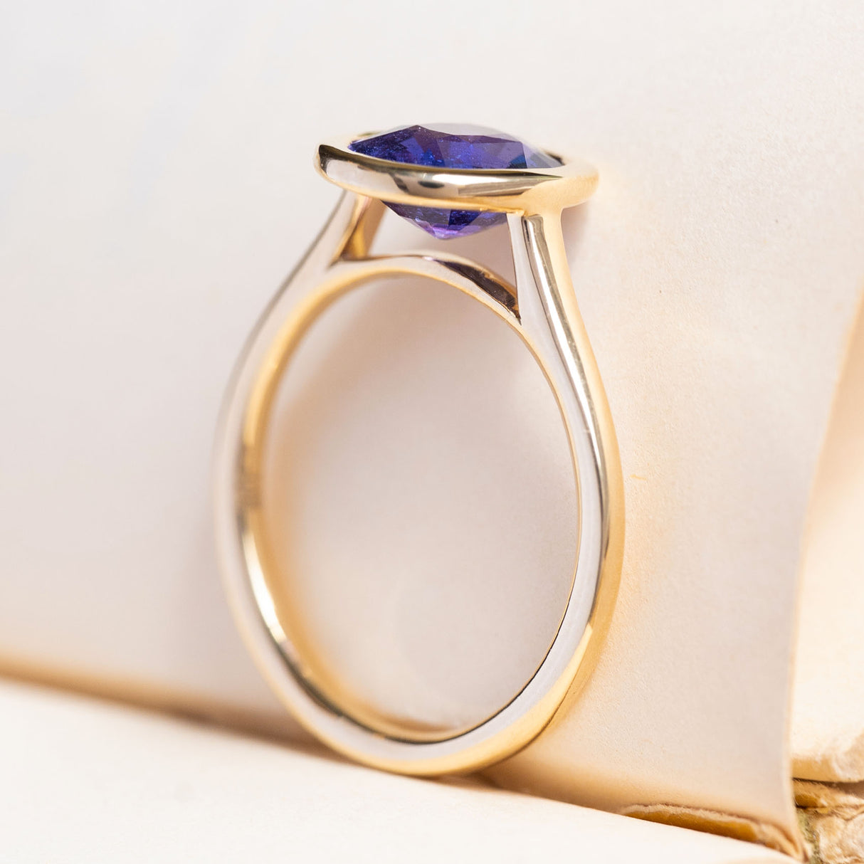 A vintage-inspired, royal purple oval sapphire solitaire ring in 14ct yellow gold with a minimalist open-back setting.