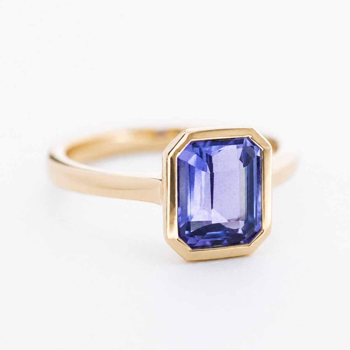 A vintage-inspired yellow gold engagement ring with a bright purple-blue sapphire at the centre.