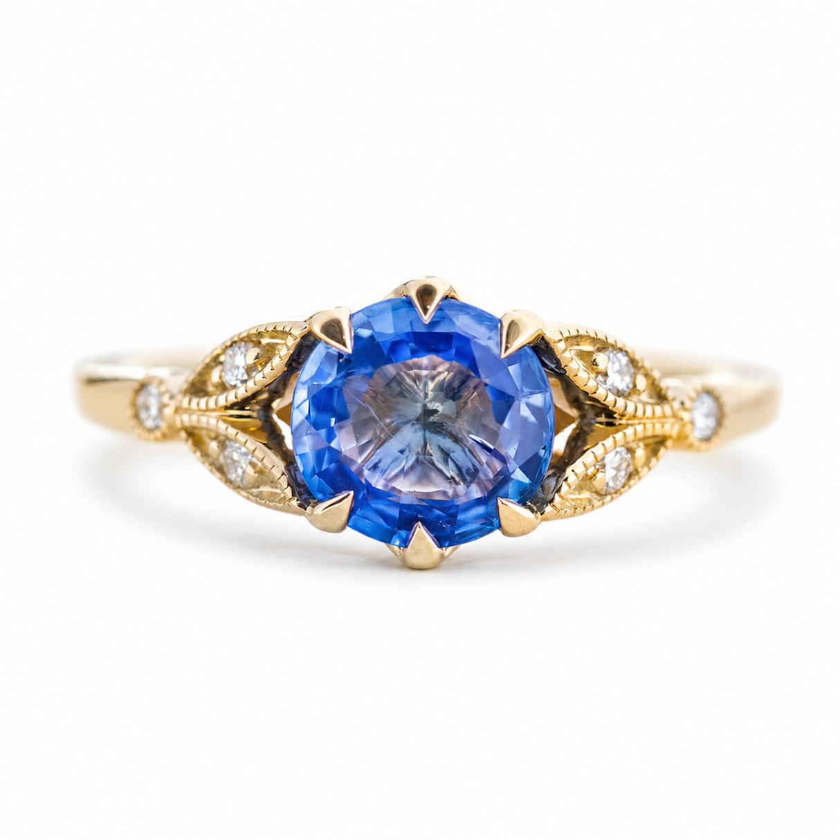 A close-up of an antique-inspired blue-purple sapphire & diamond engagement ring in yellow gold.