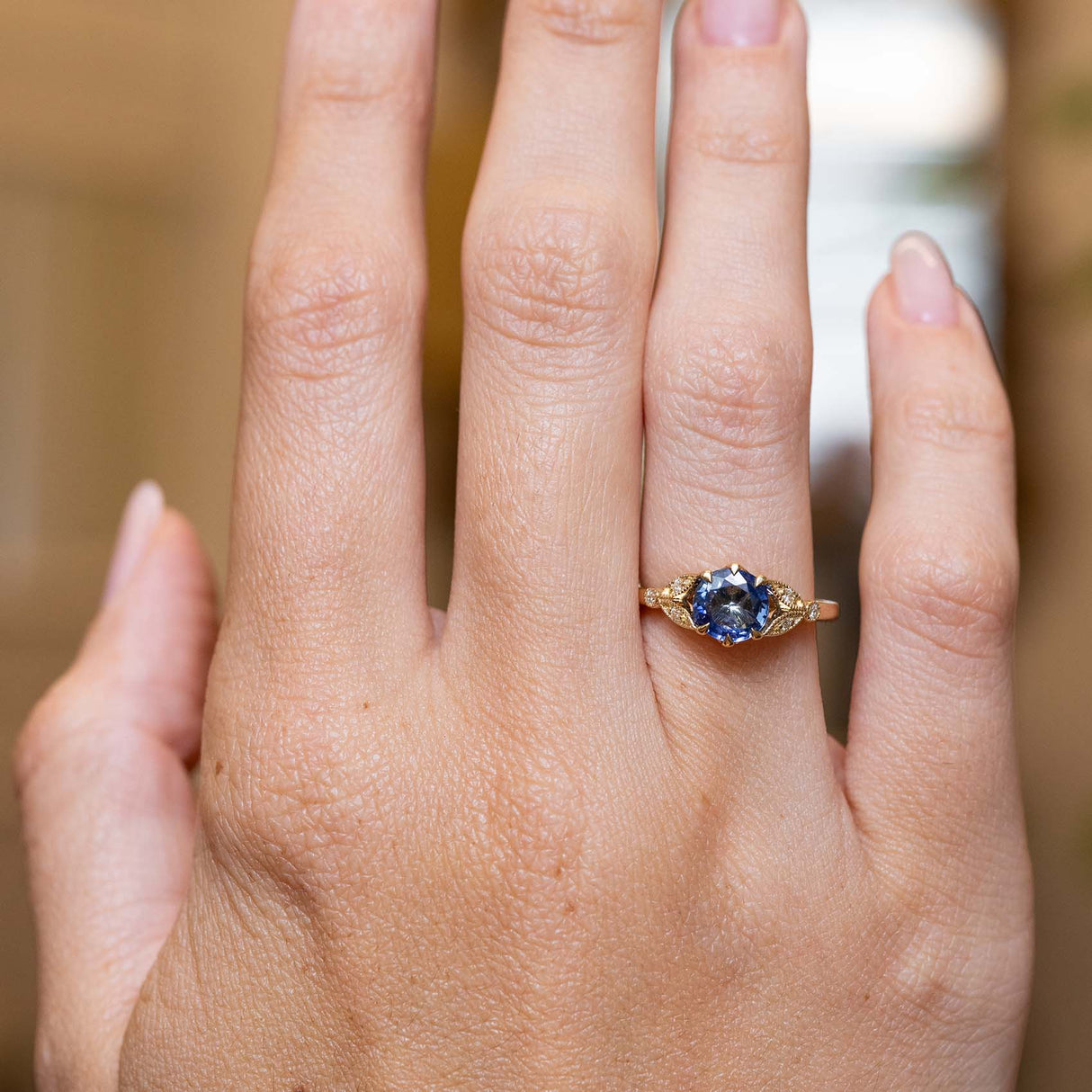 Blue-purple sapphire and diamond engagement ring showcased on the hand in a vintage-inspired yellow gold setting.