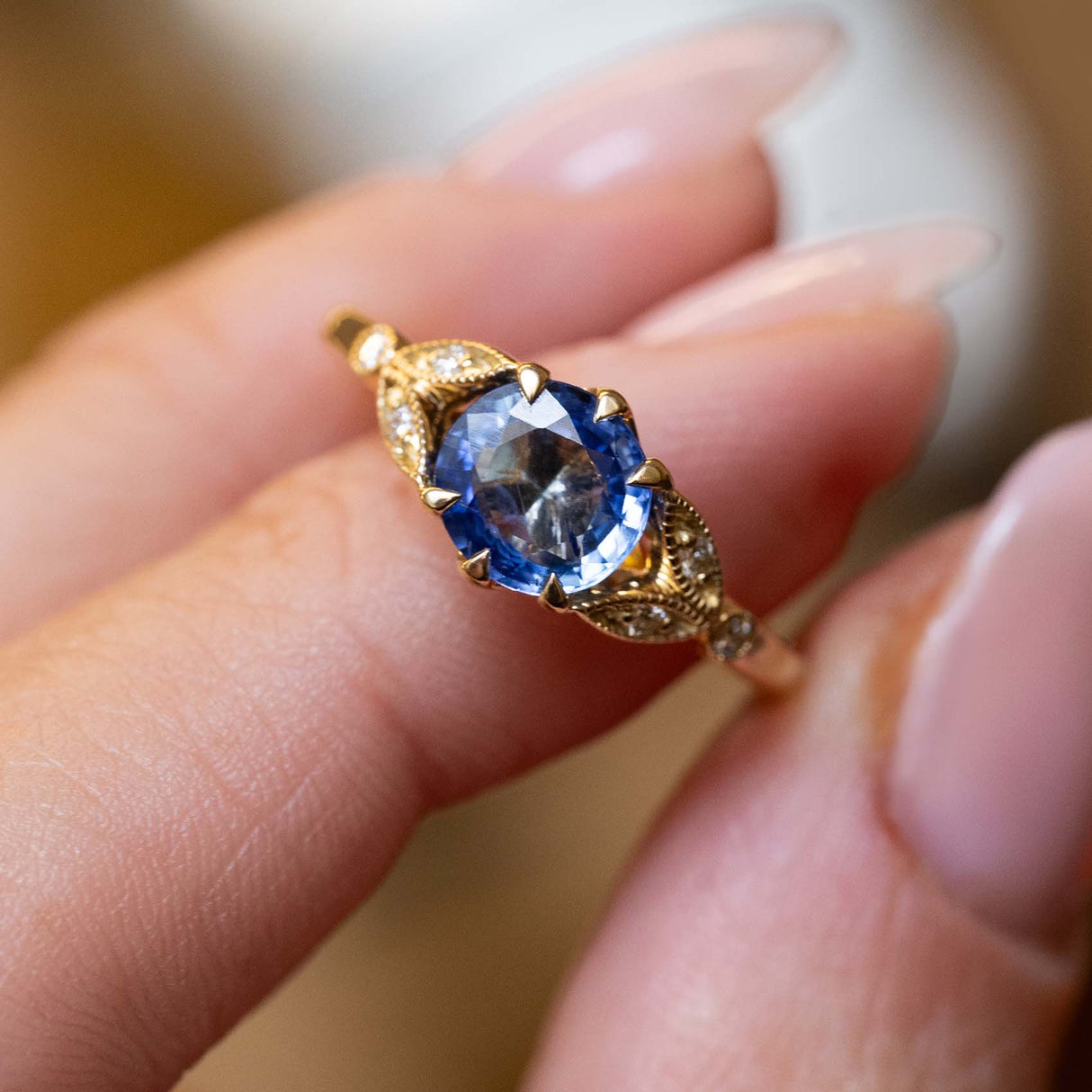 Close detail of a vintage-inspired blue-purple sapphire engagement ring with diamond accents in yellow gold.