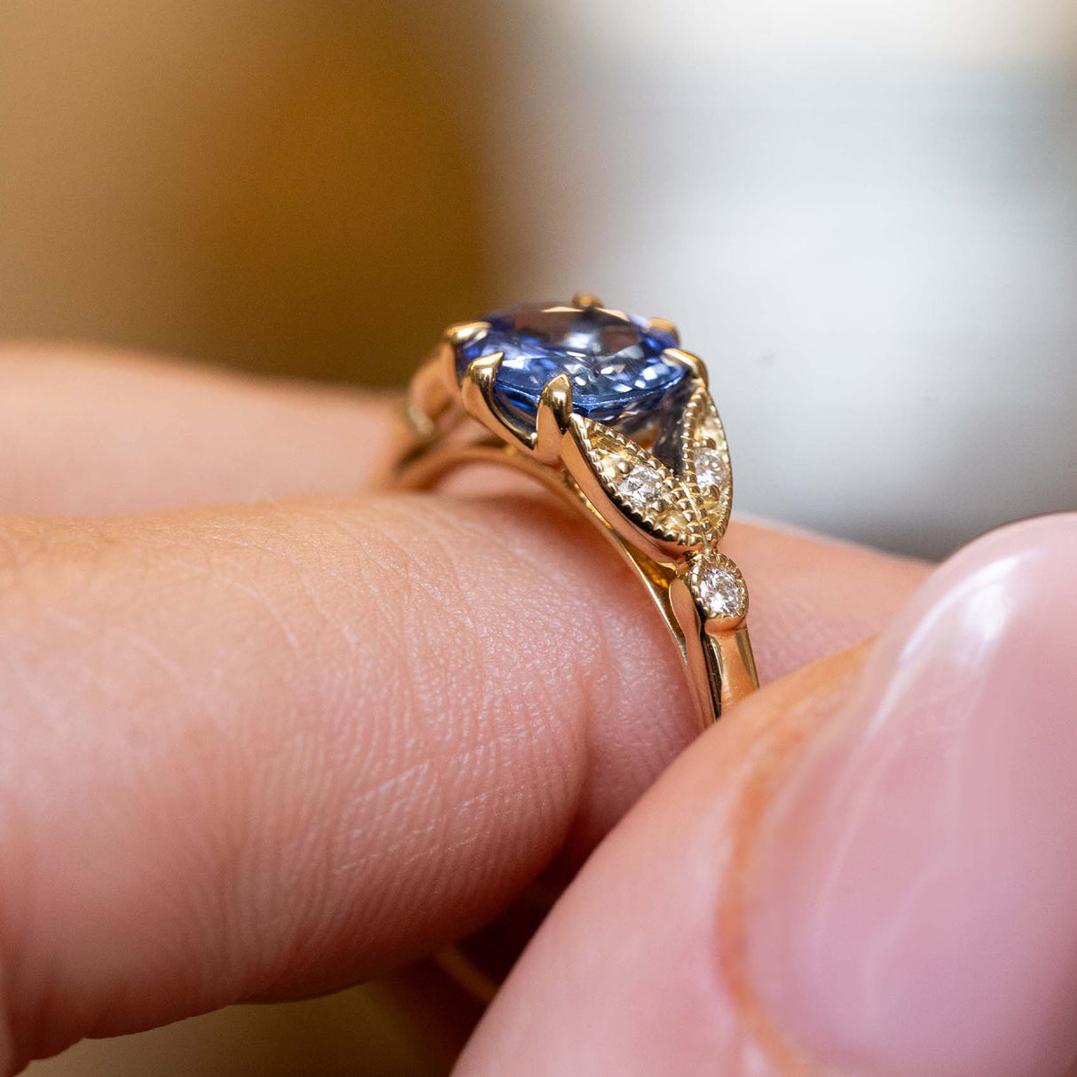 Angled detail of a vintage-inspired blue-purple sapphire and diamond engagement ring in yellow gold.