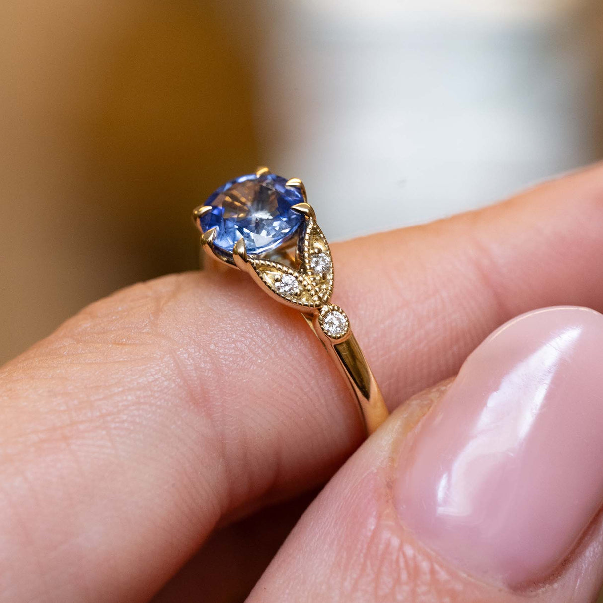 Close-up of a vintage-inspired yellow gold engagement ring featuring a blue-purple sapphire and diamond shoulders.