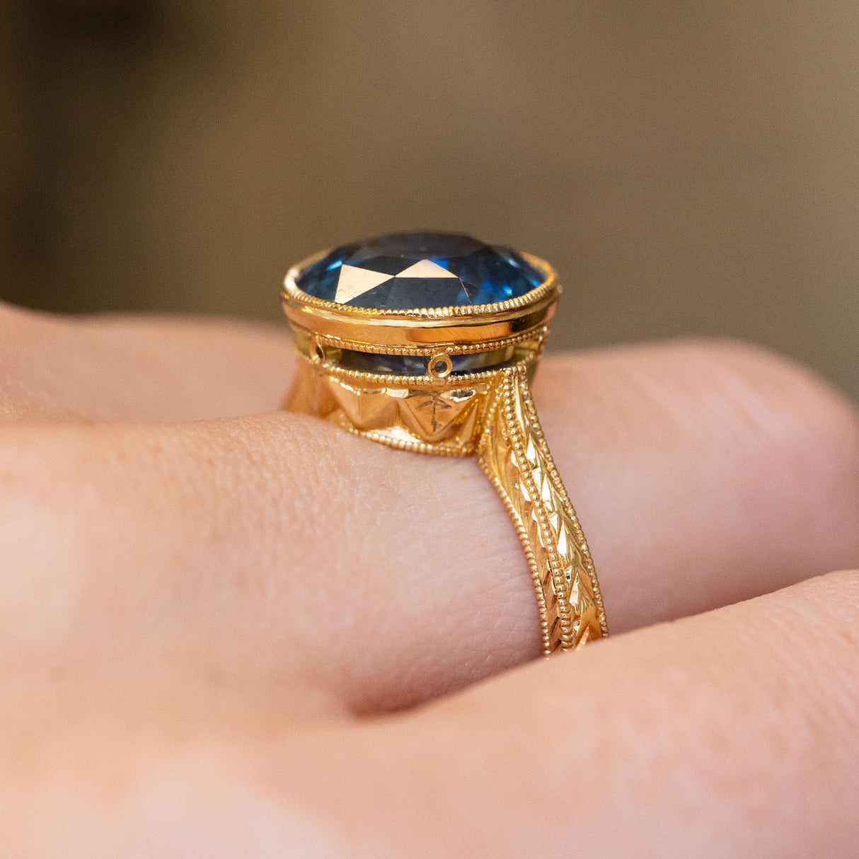 A vintage-inspired, Caribbean blue-green sapphire solitaire ring in 18ct yellow gold with intricate detailing in the gallery.