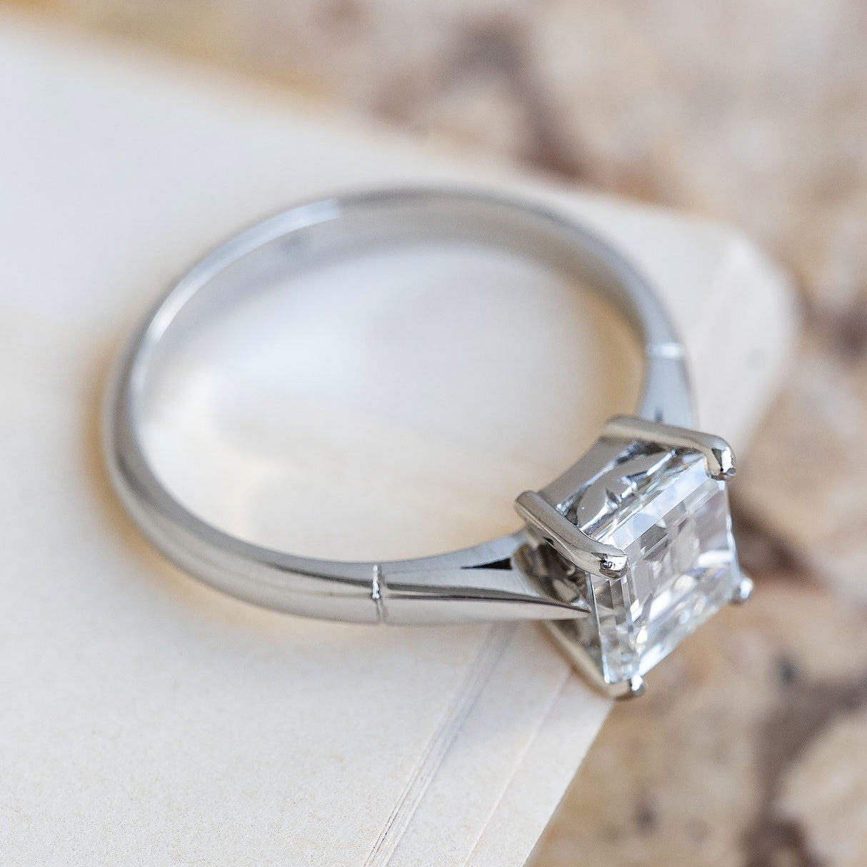 A vintage platinum solitaire claw-set diamond engagement ring displayed on a book.