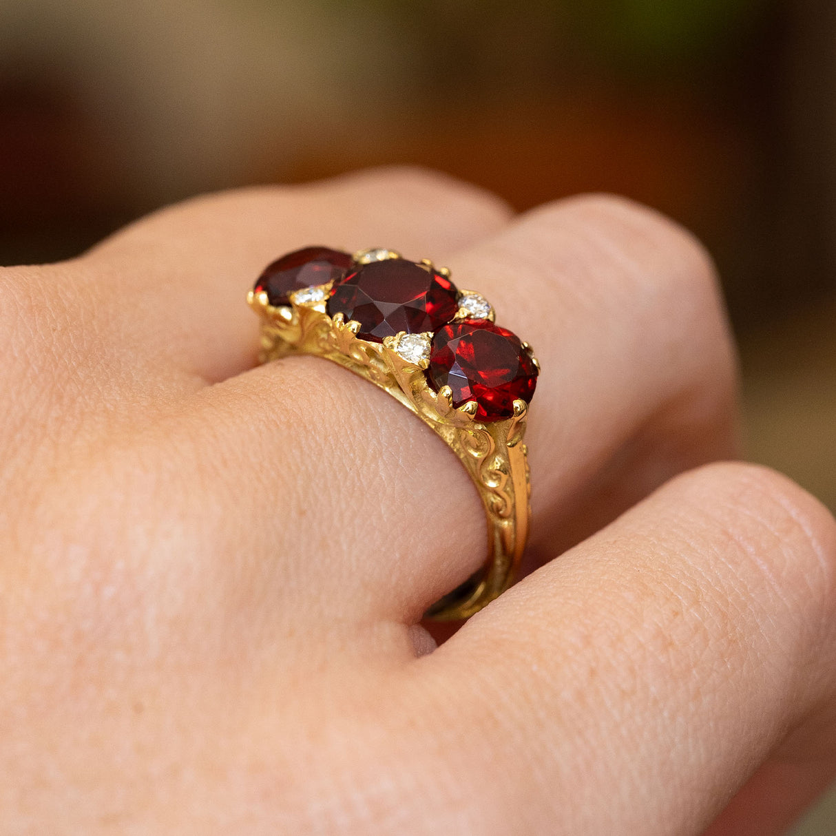 A vintage three-stone garnet with a deep red hue set in carved yellow gold with scroll details in the gallery.