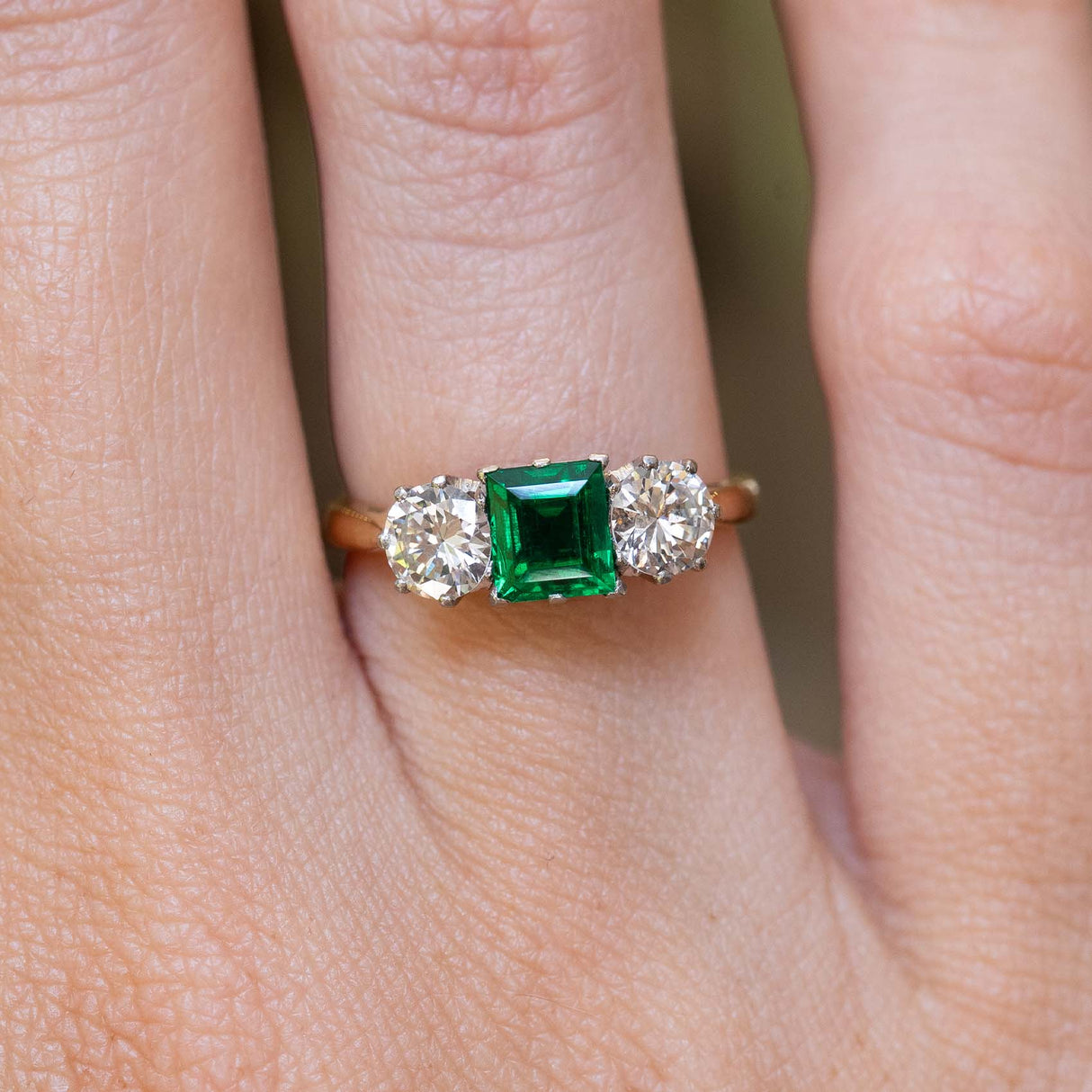 A vintage 1960s emerald and diamond three-stone ring worn on the finger.