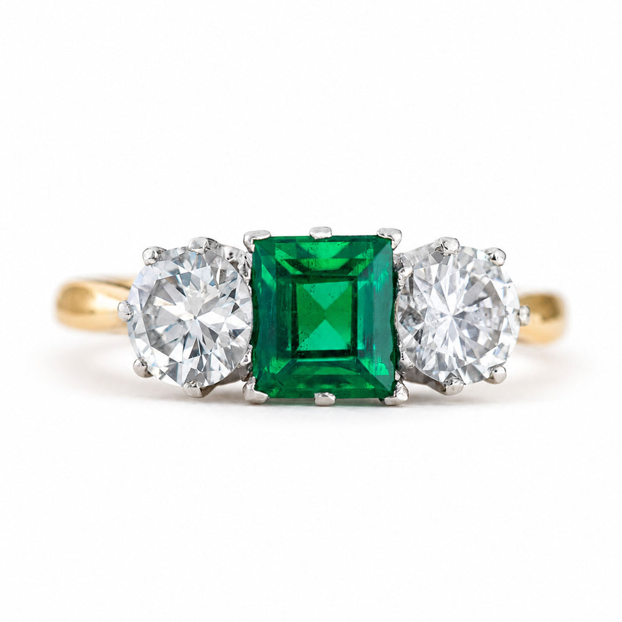 A close-up of a Vintage, 1960s emerald and diamond three-stone ring with a yellow gold band.
