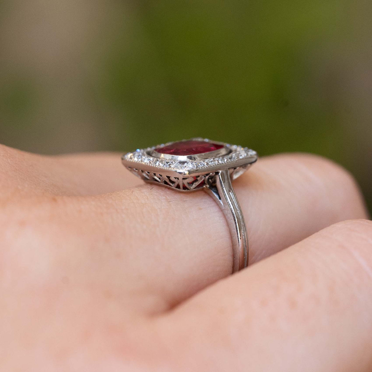 Side detail of an antique Art Deco red spinel and diamond cluster ring worn on the finger.