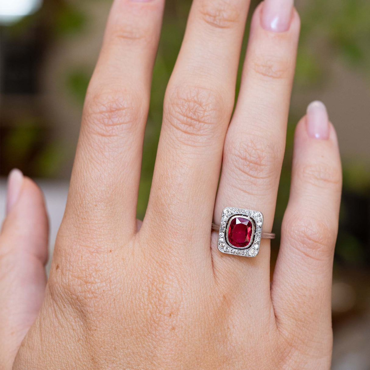 An antique Art Deco red spinel and diamond cluster ring worn on the hand.