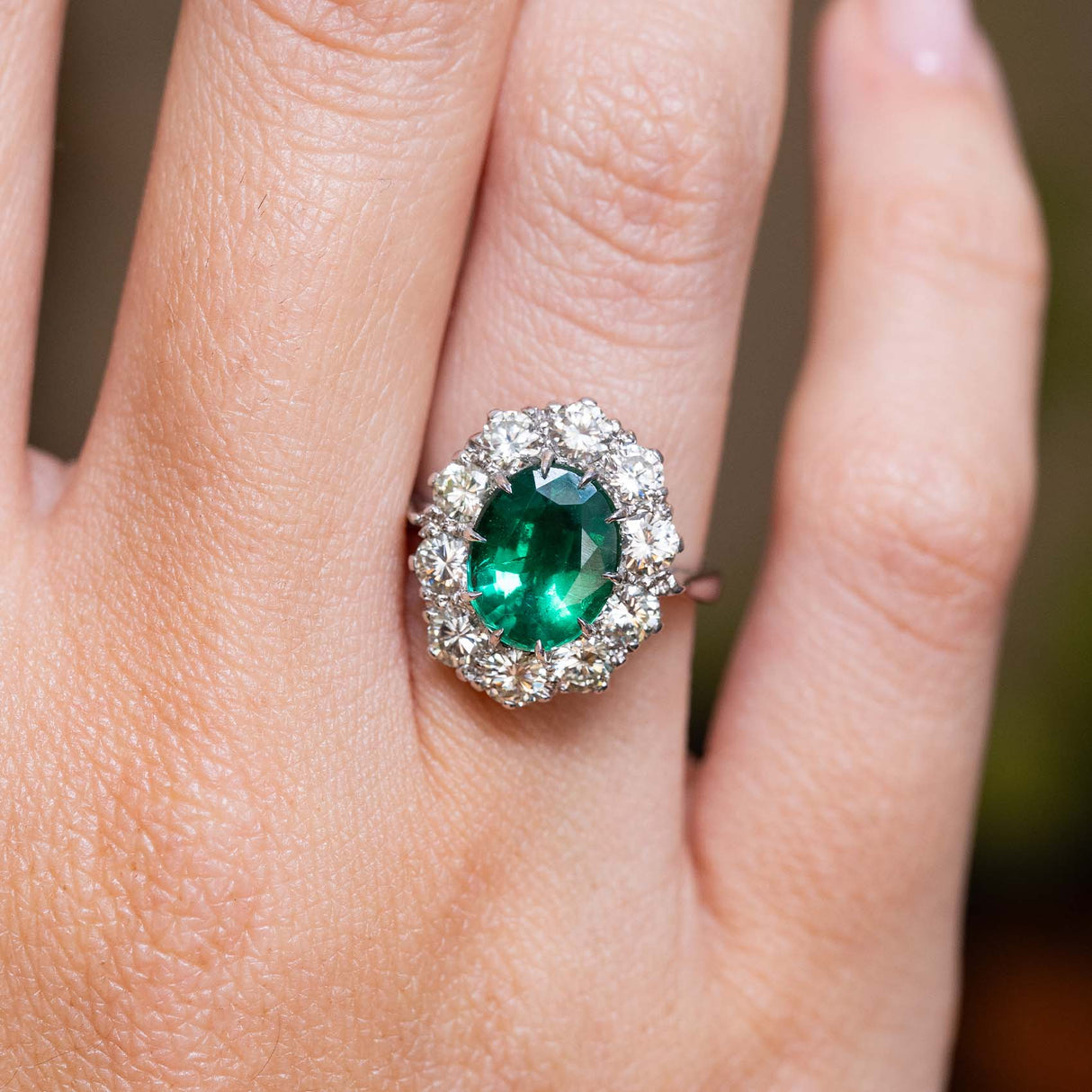 Vintage 1950s oval-cut emerald and diamond cluster engagement ring in white gold worn on the finger.