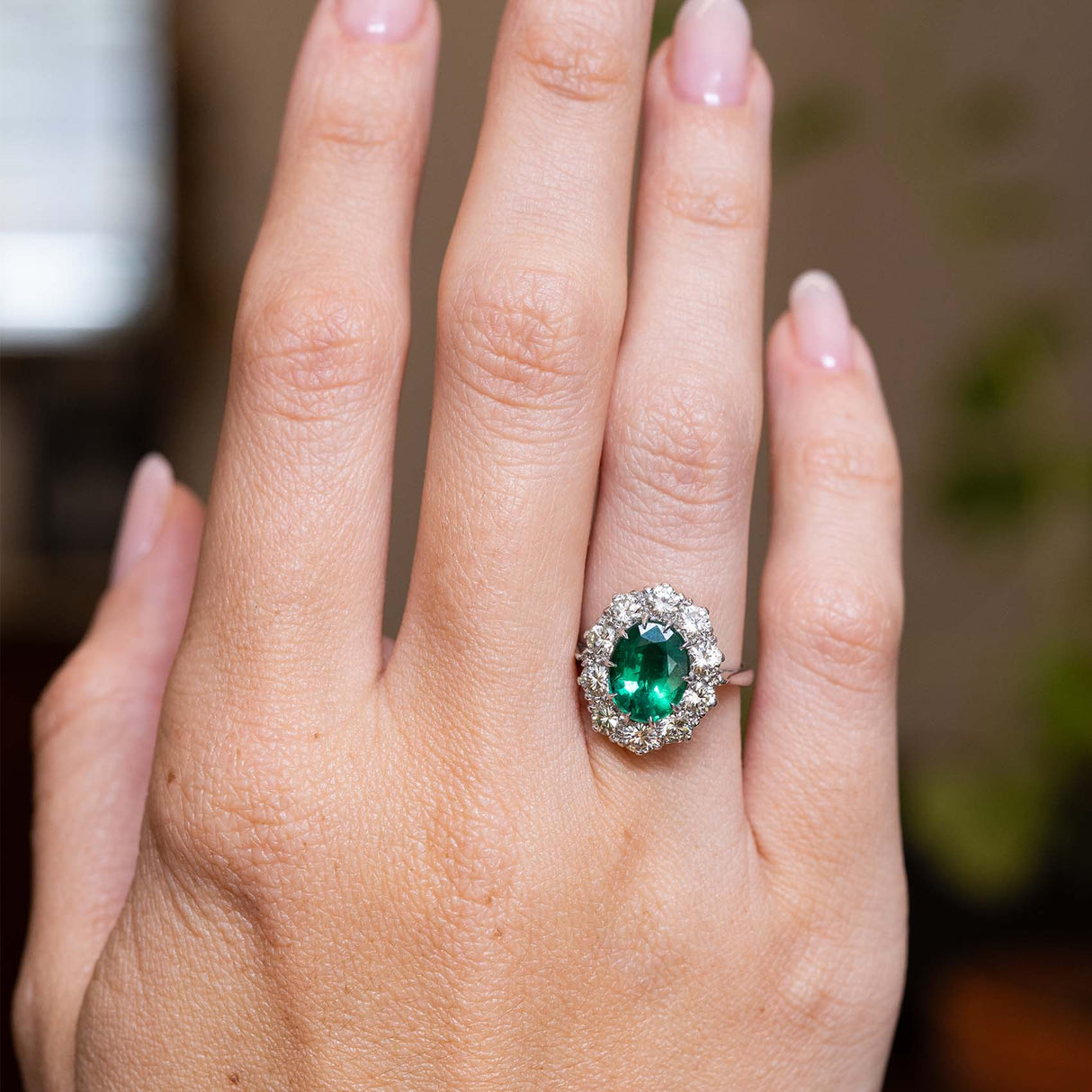 Vintage 1950s oval-cut emerald and diamond engagement ring showcased on the hand in white gold.