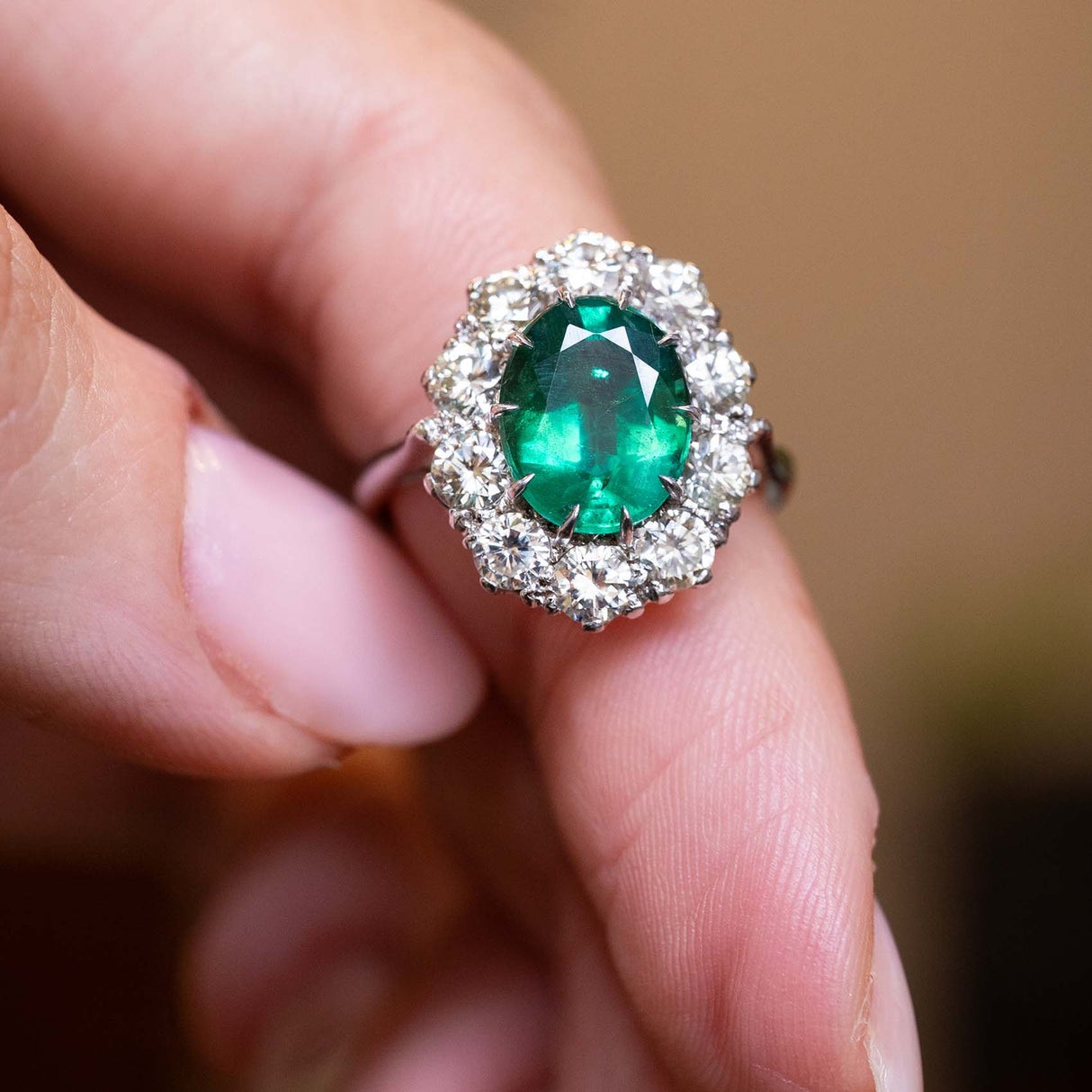 Oval-cut emerald surrounded by a diamond cluster in a vintage 1950s white gold engagement ring.