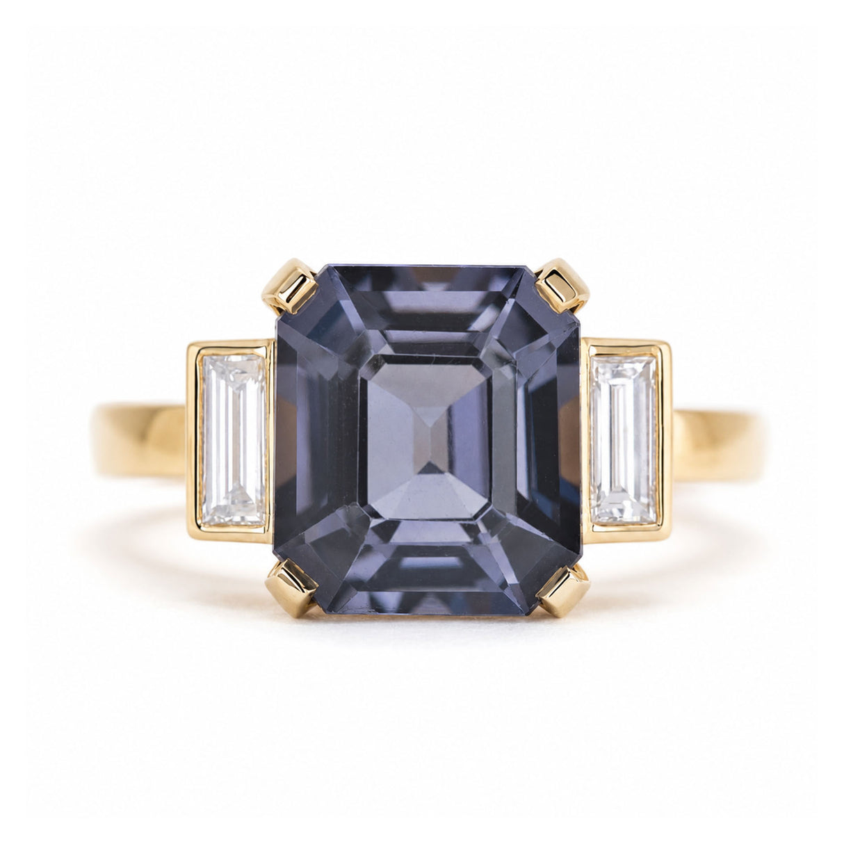 A close-up of a vintage-inspired, Blue spinel and diamond three-stone engagement ring in 14ct yellow gold.