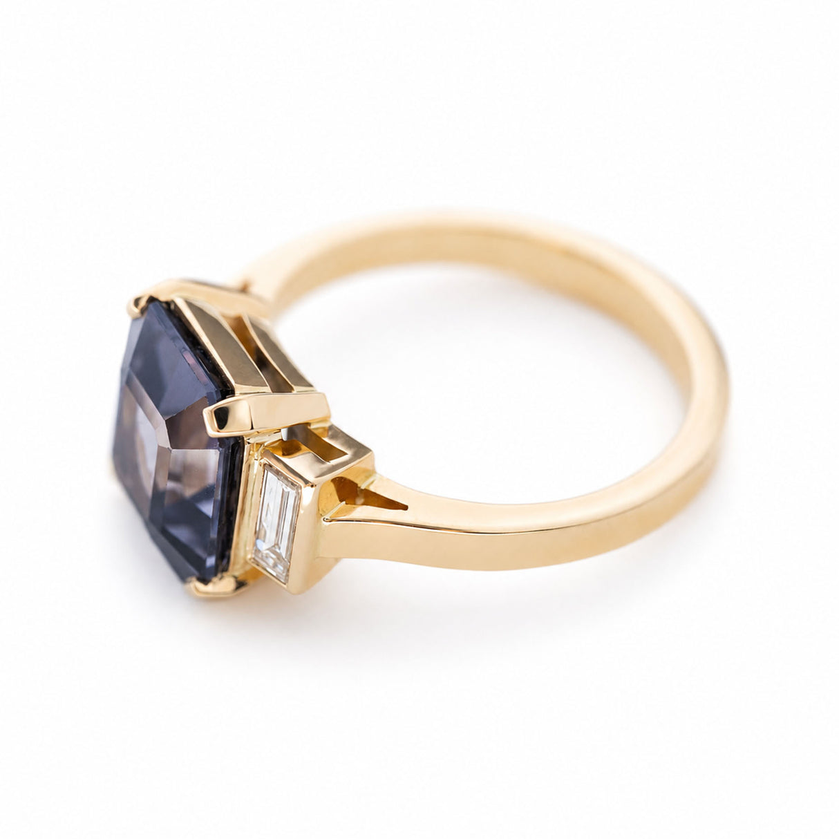 A vintage-inspired engagement ring featuring a blue spinel flanked by baguette diamonds set in yellow gold.