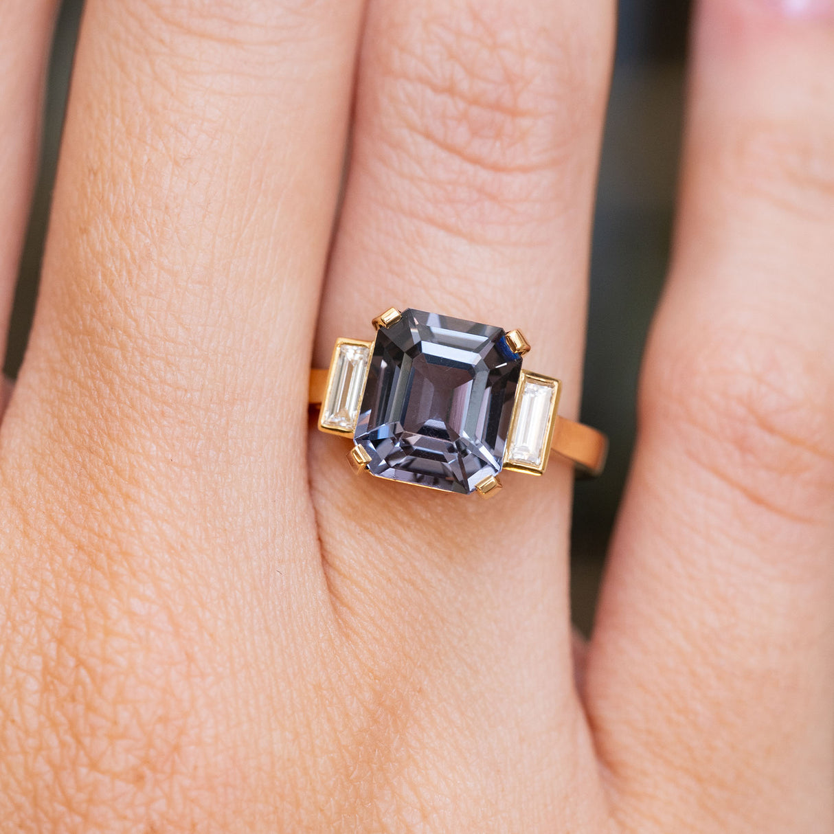 Blue spinel and baguette diamond engagement ring worn on the finger
