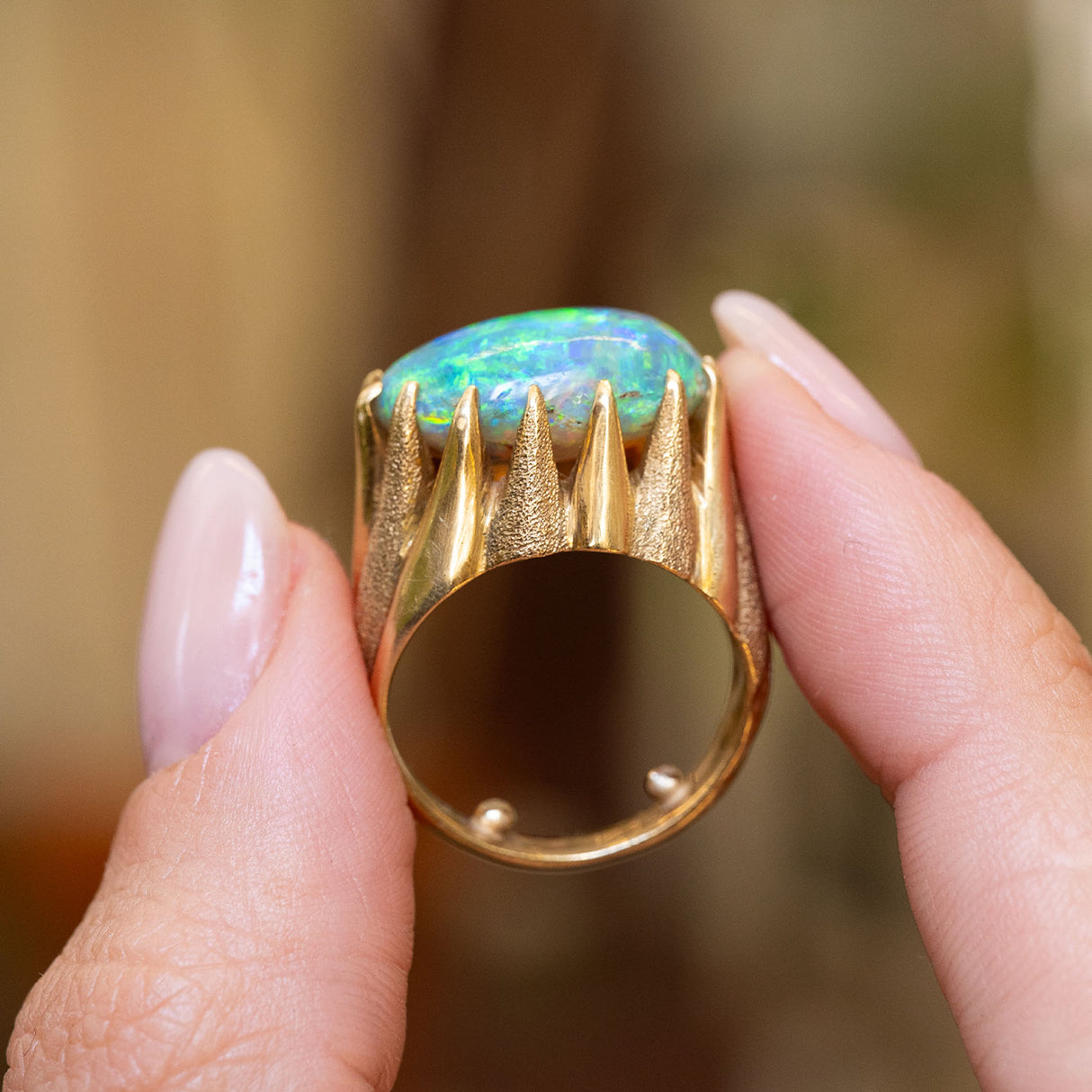 A close-up of a 18ct yellow gold, vintage 1970s cabochon Australian opal ring held between the fingers.